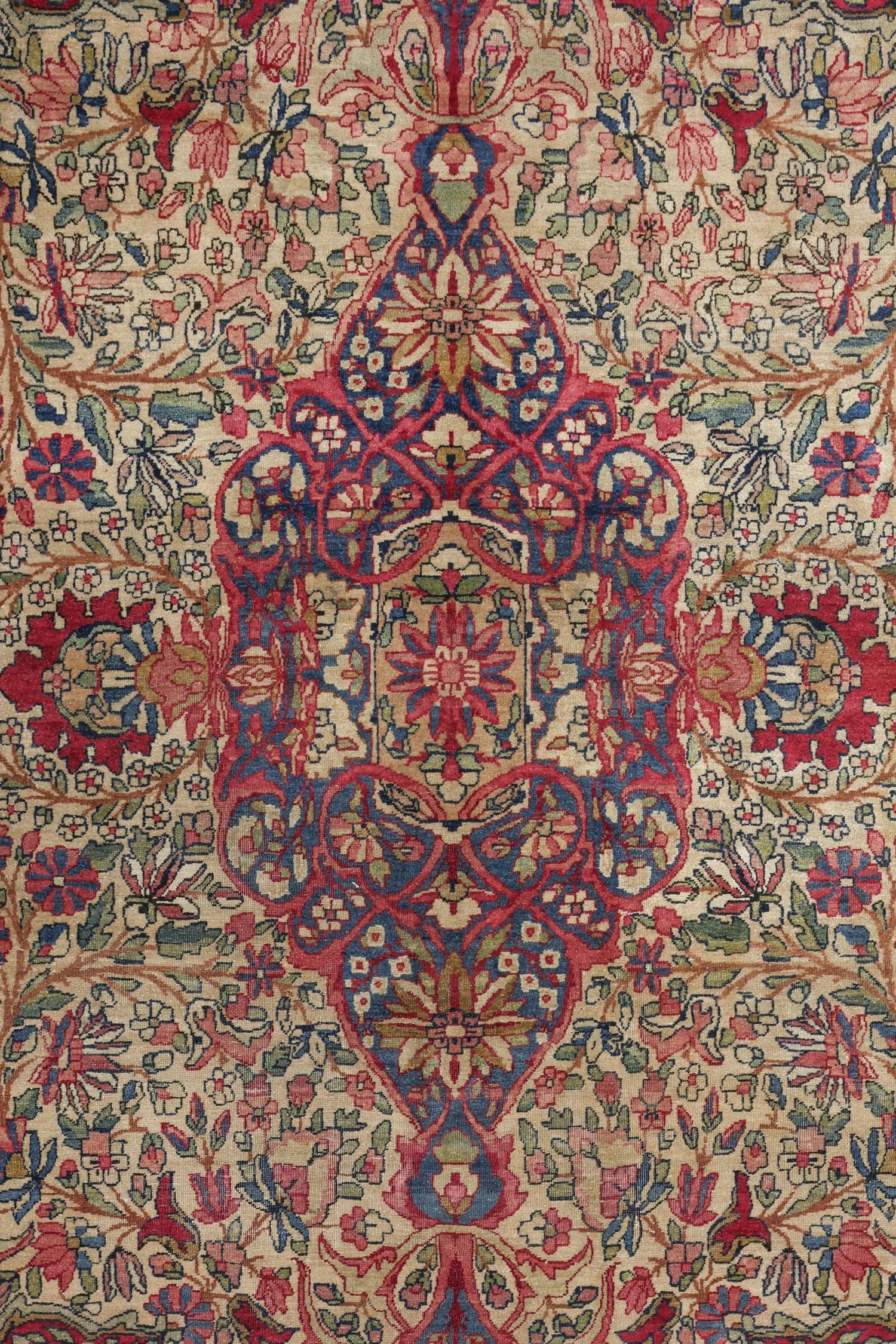 Detail of antique Kerman rug, showcasing a floral and medallion design in red, blue, and beige tones.
