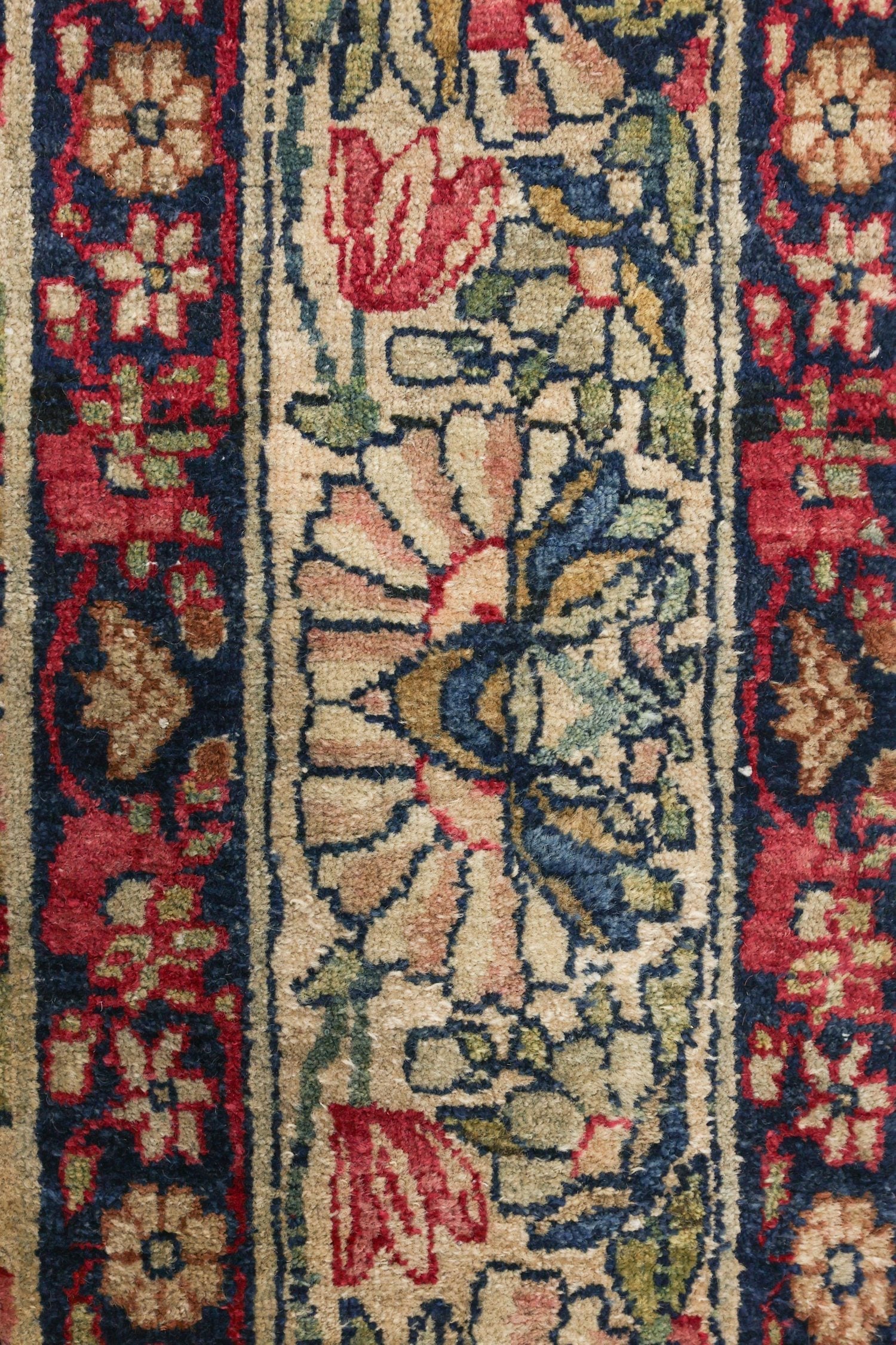 Close-up detail of a traditional handwoven rug, showcasing its intricate floral pattern in shades of red, beige, and navy.
