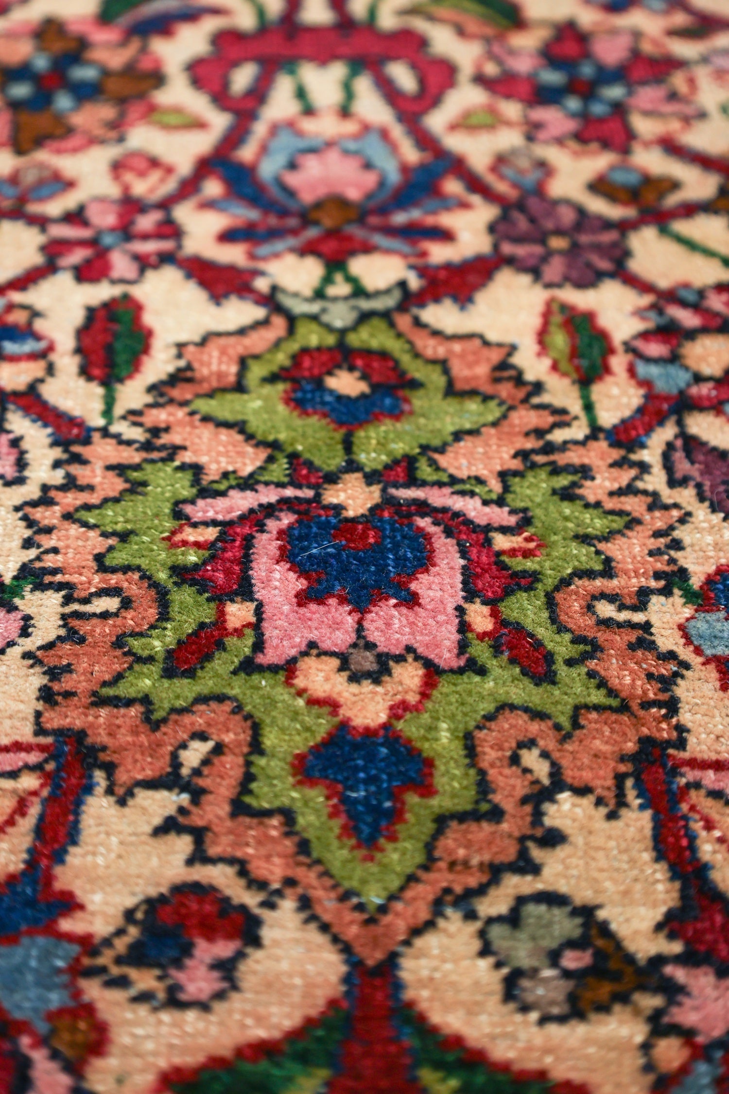 Close-up of a traditional rug's detailed floral pattern in rich reds, greens, and blues on a cream background.
