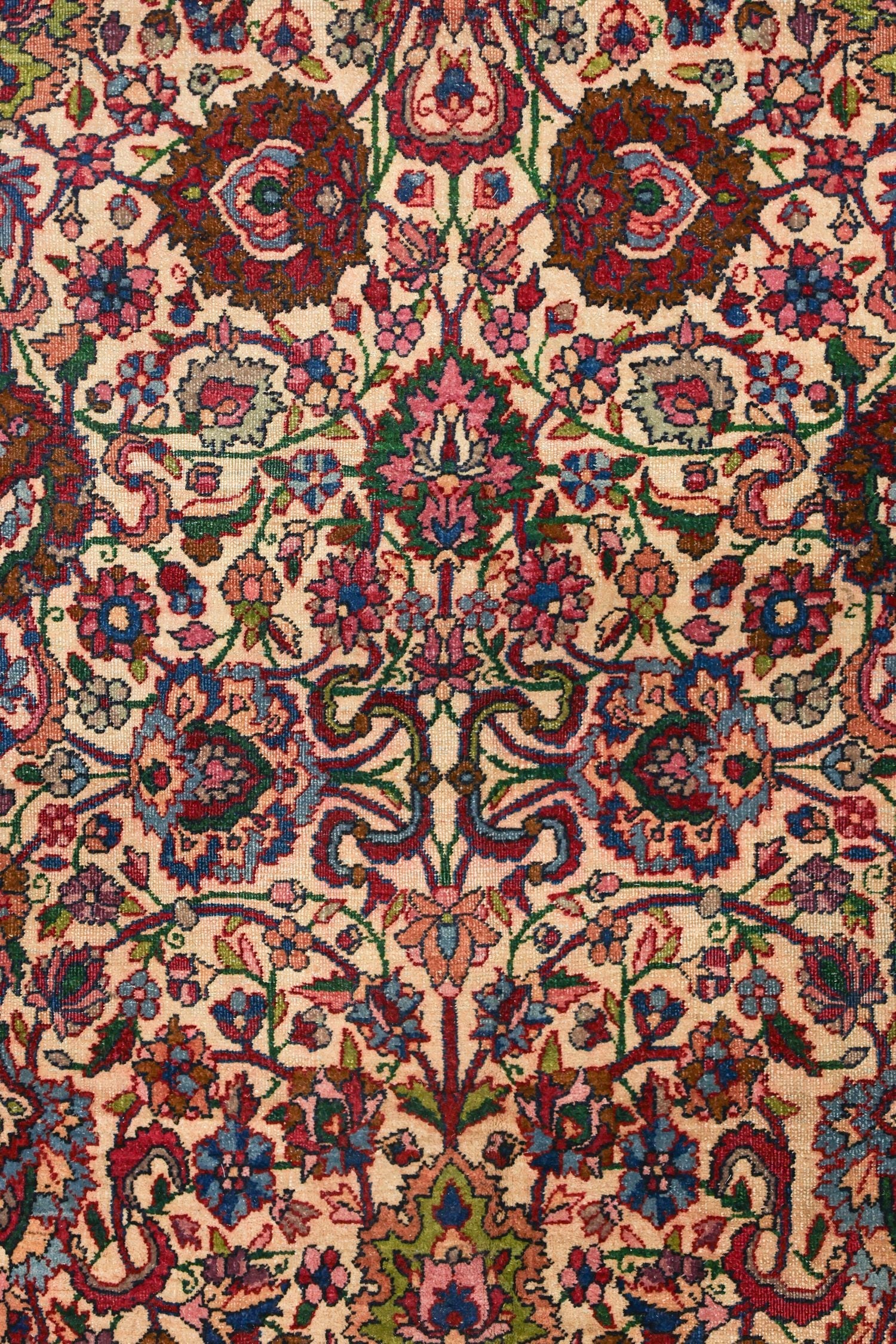 Close-up of a handwoven antique rug, showcasing intricate floral patterns in rich jewel tones on a creamy background.
