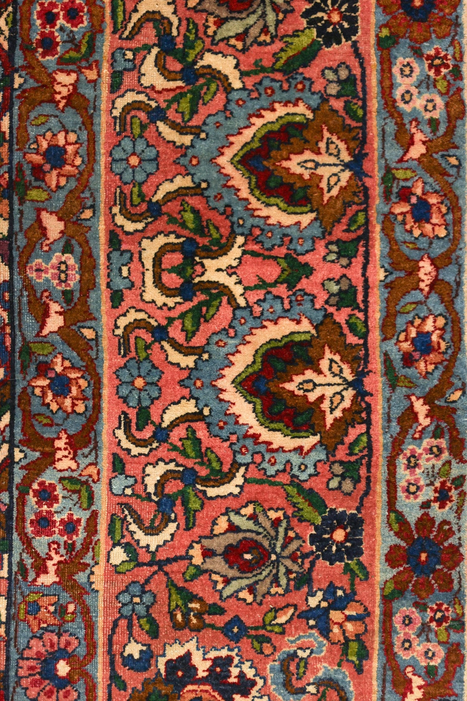 Close-up detail of a traditional handwoven rug, showcasing intricate floral patterns in muted pink, blue, and green hues.
