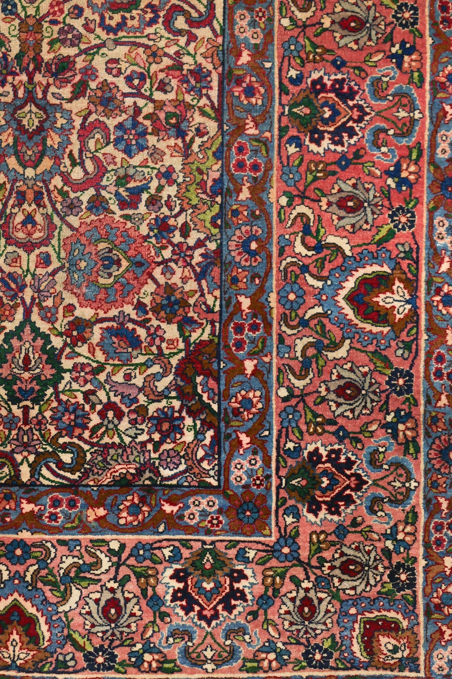 Detail of a traditional handwoven rug with a pink and blue floral pattern.
