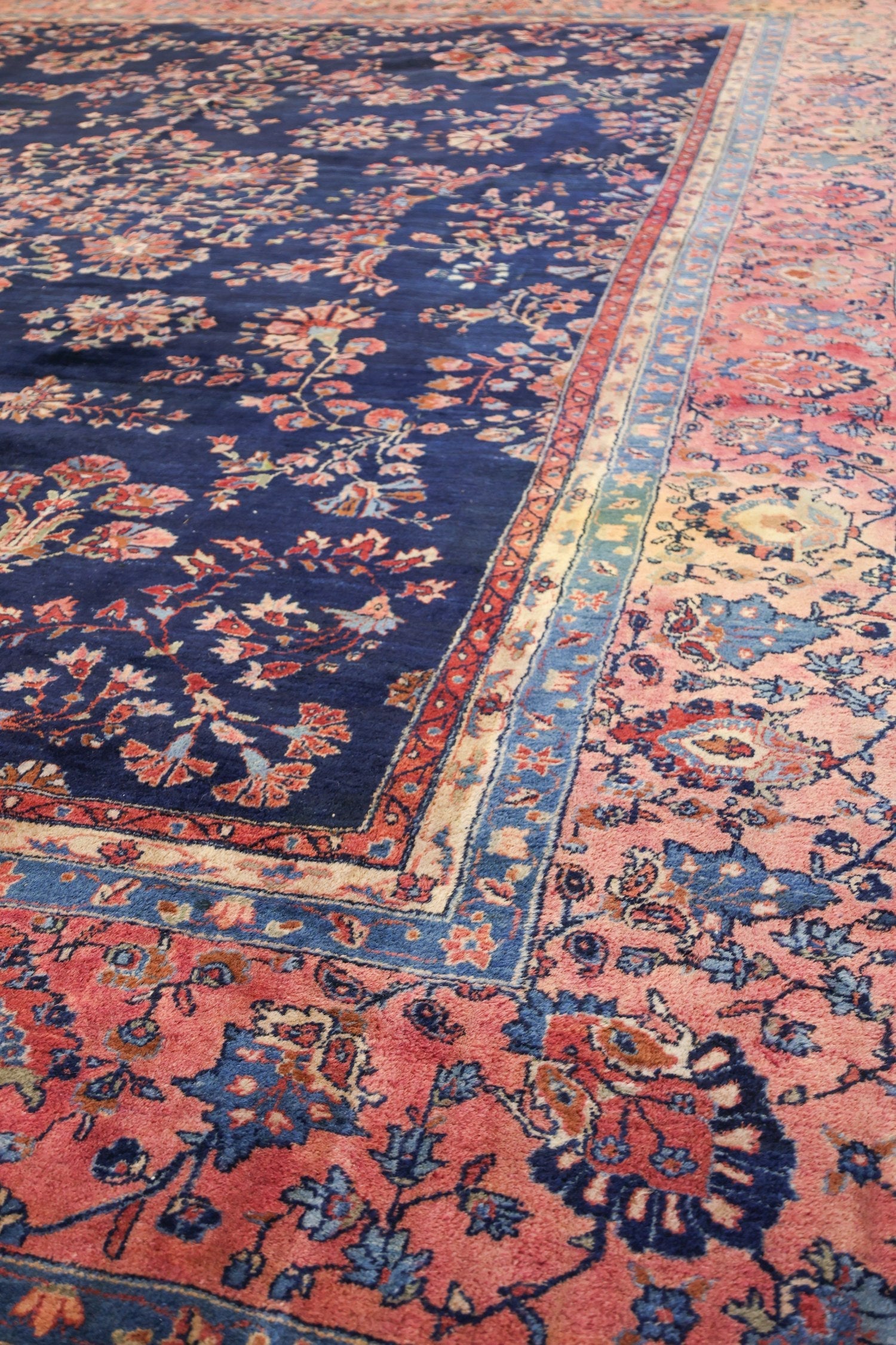 Handwoven antique rug detail, showcasing a navy blue field with pink floral border.
