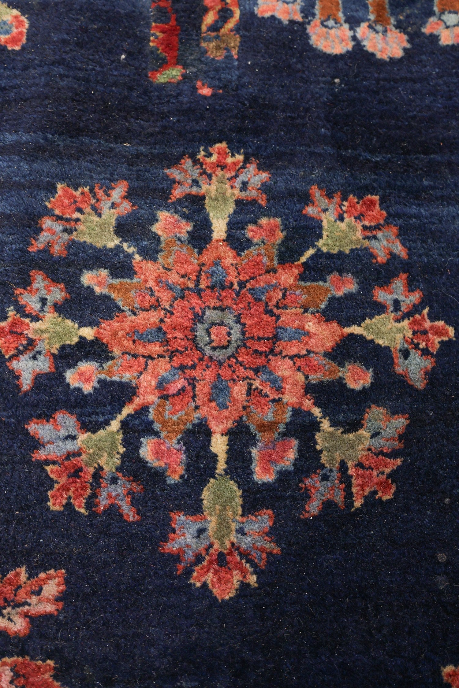 Detail of antique rug's handwoven floral pattern in navy and reds.
