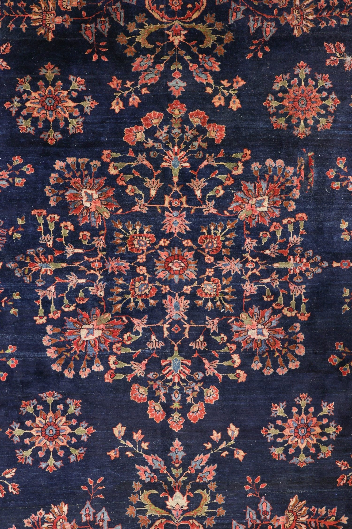 Intricate navy blue rug detail; handwoven floral pattern in muted reds and greens.
