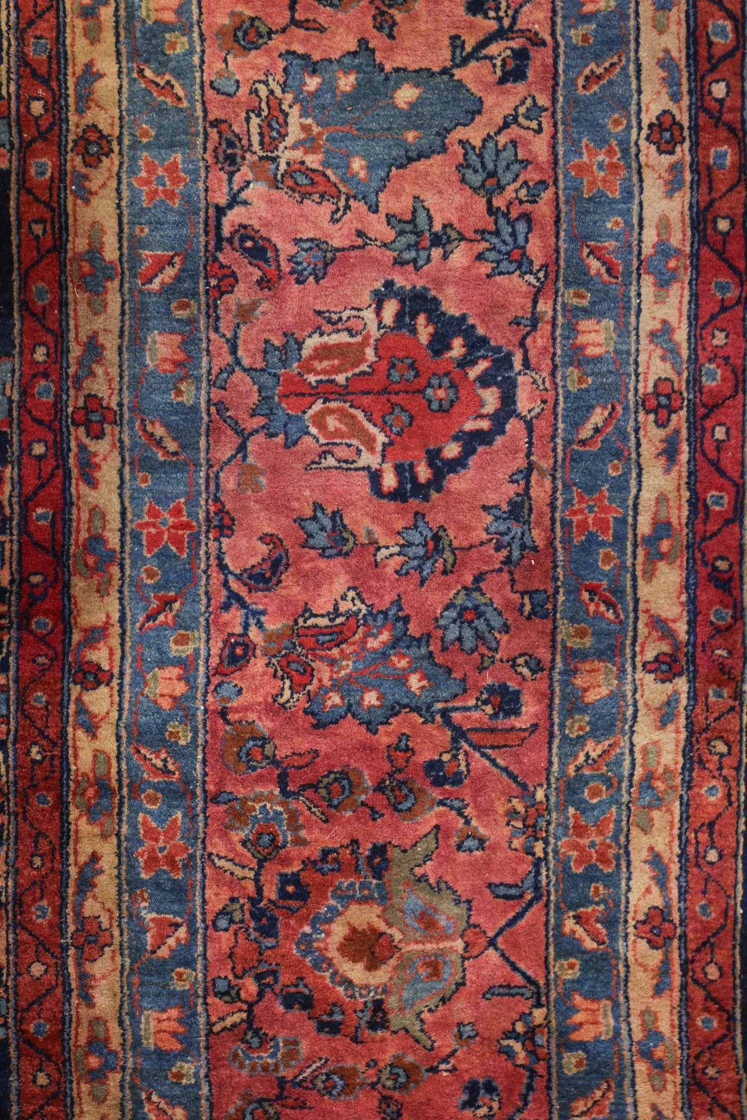 Detail of a traditional handwoven rug, showcasing a red and blue floral pattern with intricate border.
