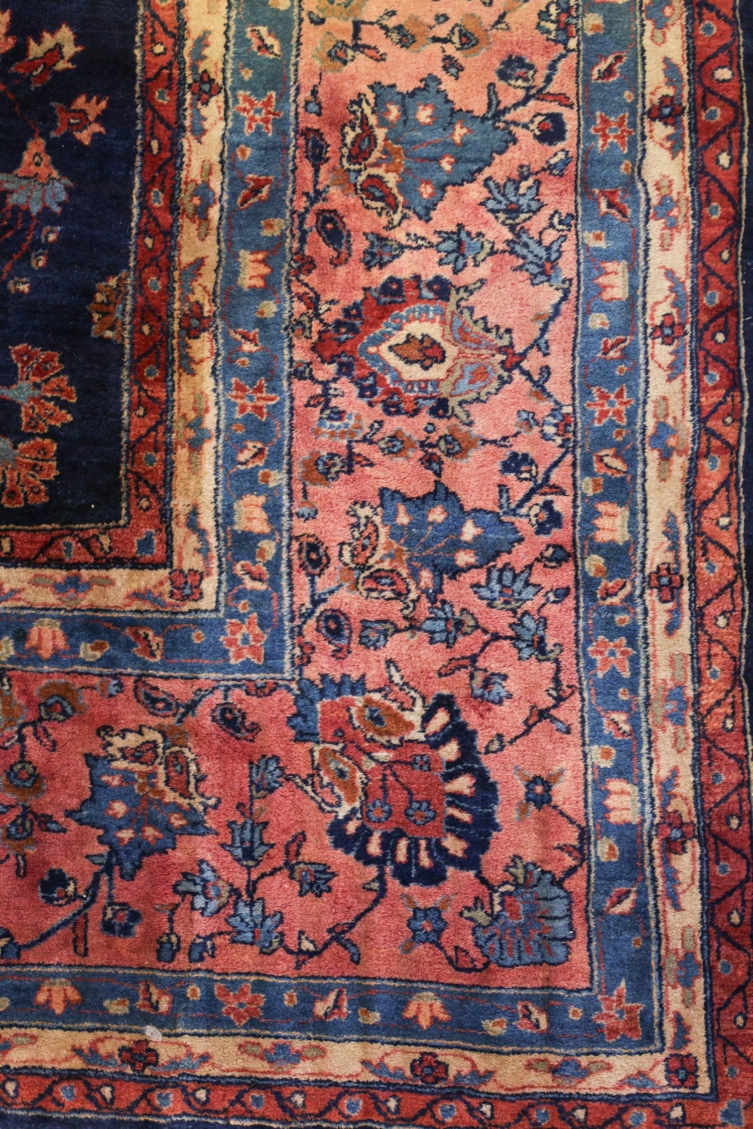 Antique rug detail: handwoven Sarouk carpet with intricate floral pattern in shades of red, blue, and beige.
