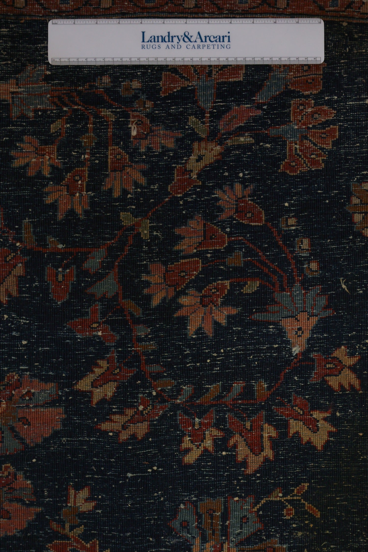 Close-up detail of antique rug's navy blue field with reddish-pink floral pattern, showing handwoven texture.
