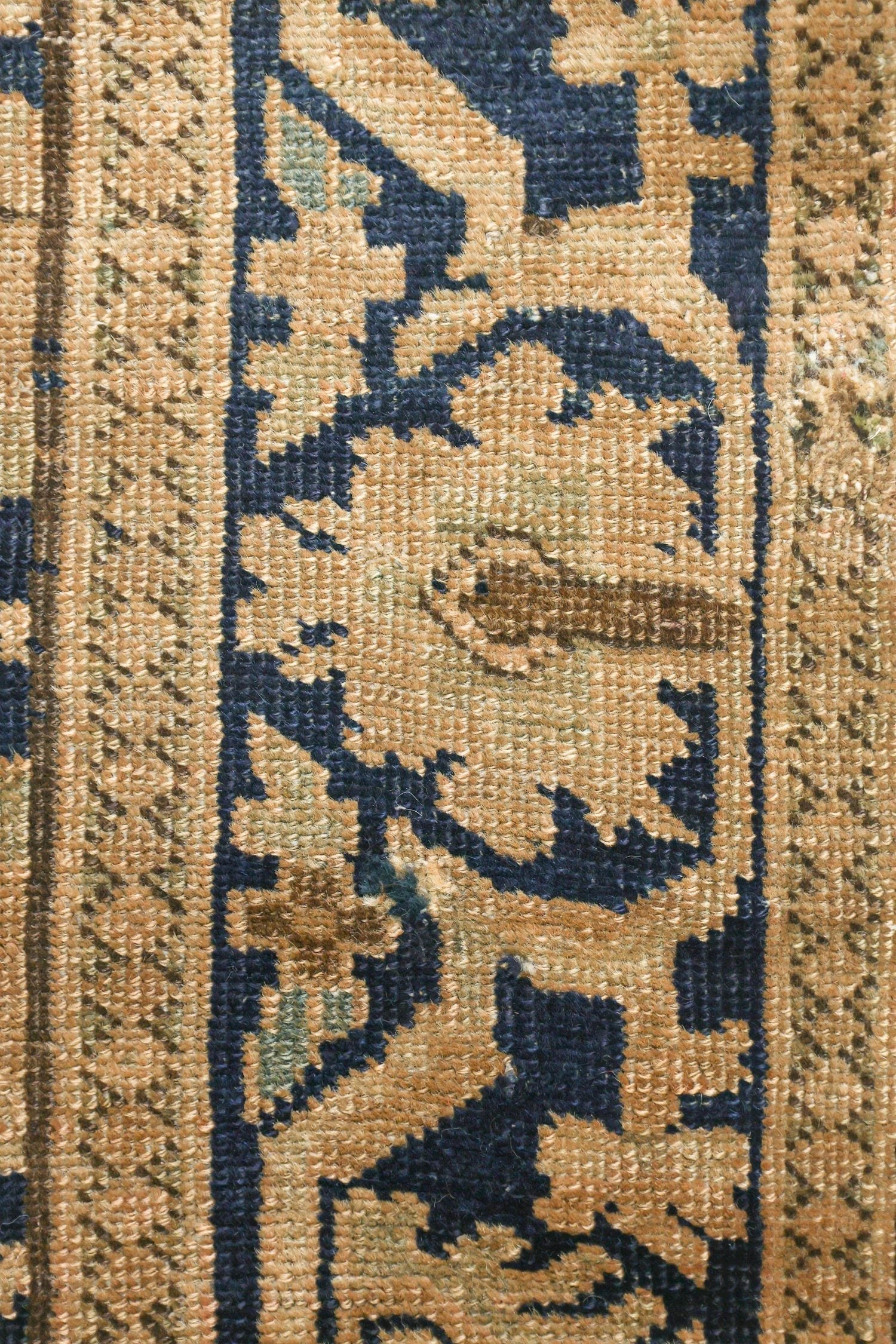 Close-up detail of antique rug's handwoven pattern, showcasing beige and navy blue tones.
