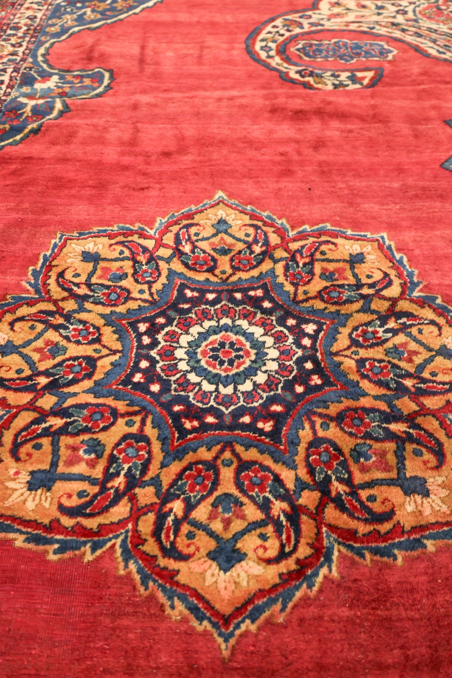 Intricate detail of a handwoven rug, showcasing a crimson field with a navy blue and gold floral medallion.
