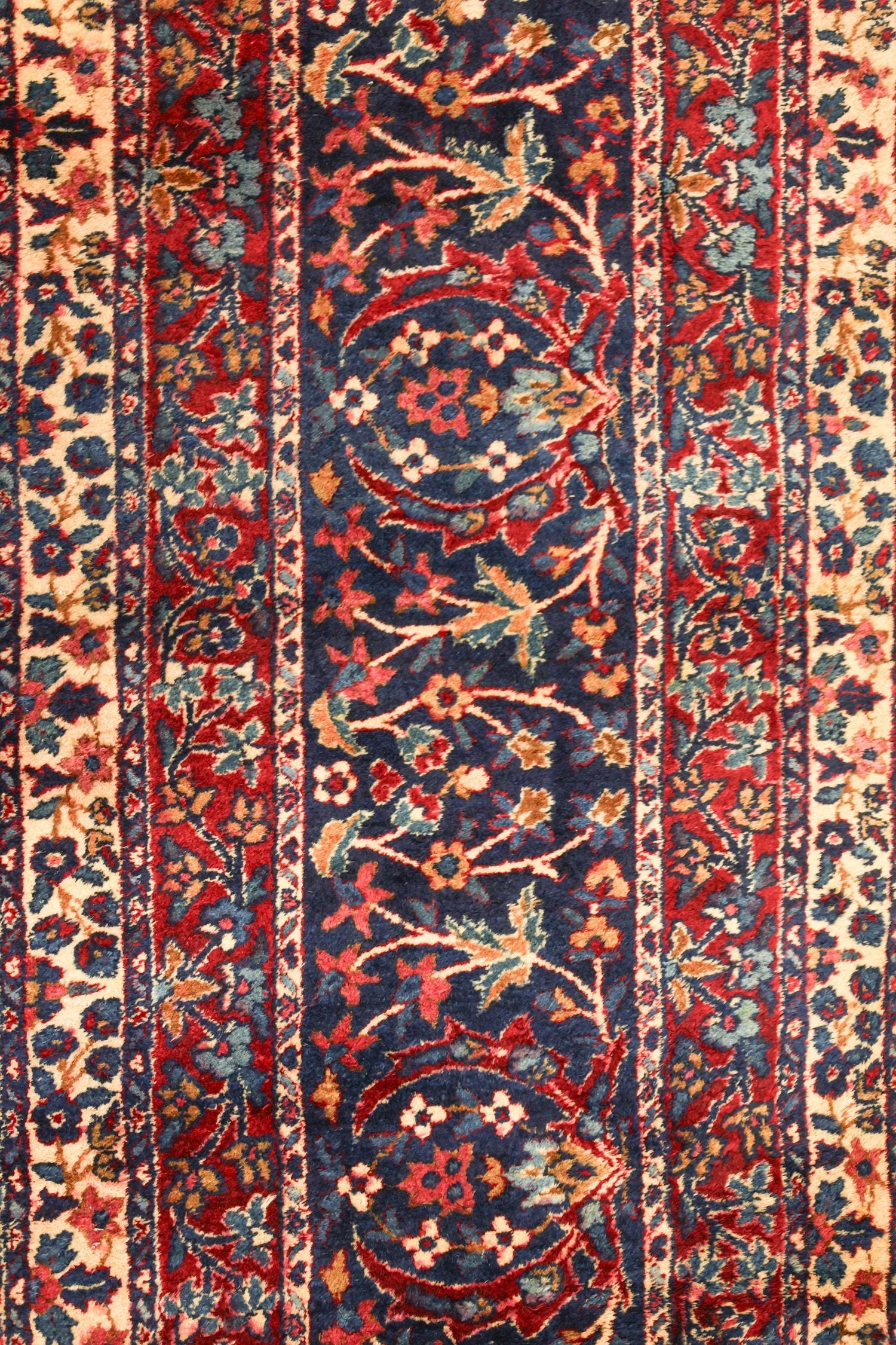 Detail of antique Kerman rug, showcasing its intricate floral pattern in rich reds, blues, and creams.
