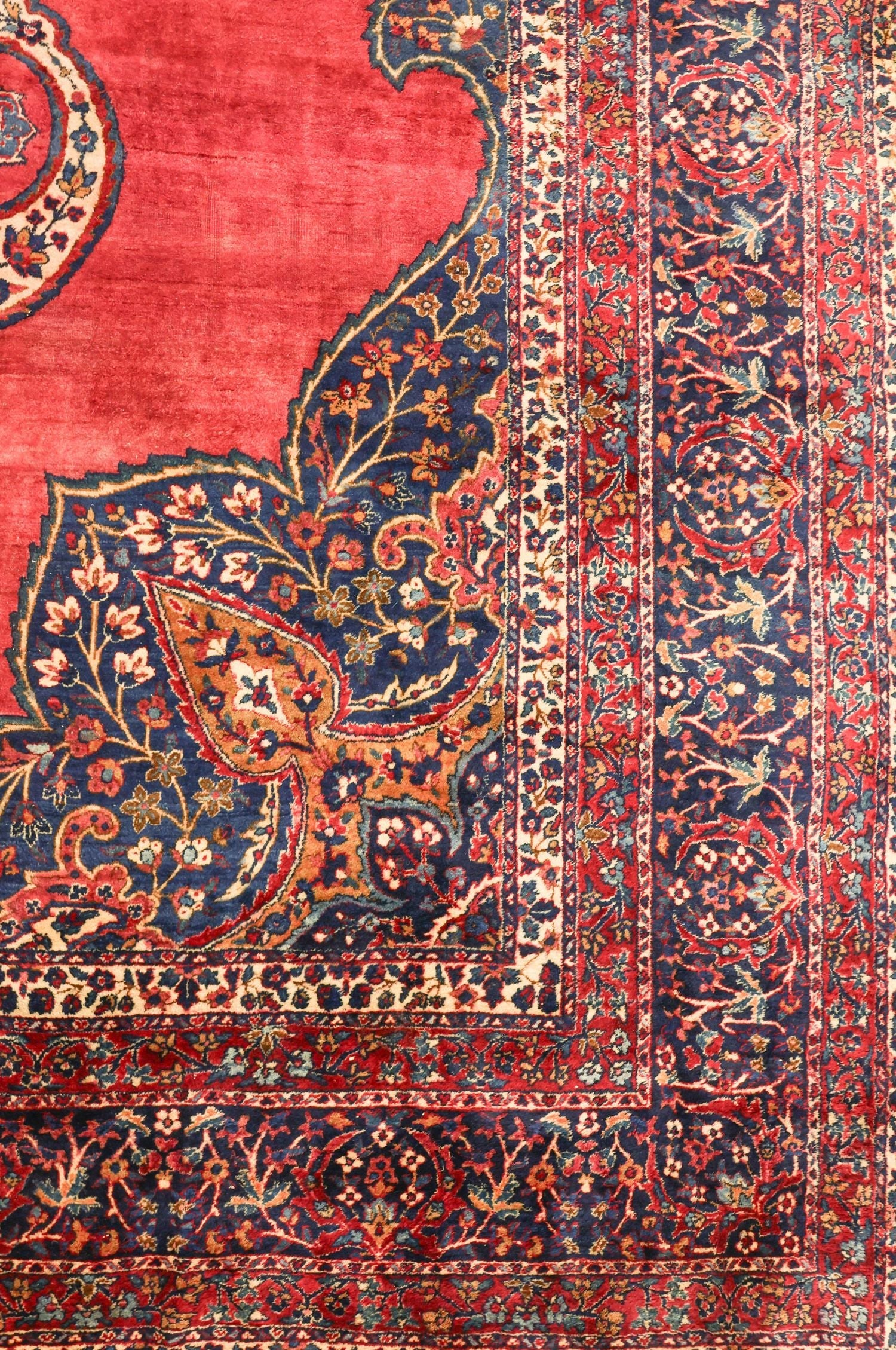 Detail of a handwoven rug's intricate floral border, showcasing rich red and navy tones.
