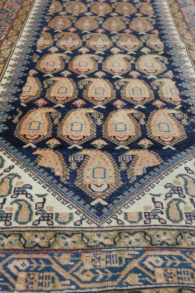 Detail of antique Afshar rug; navy blue field with beige paisley pattern, off-white border.
