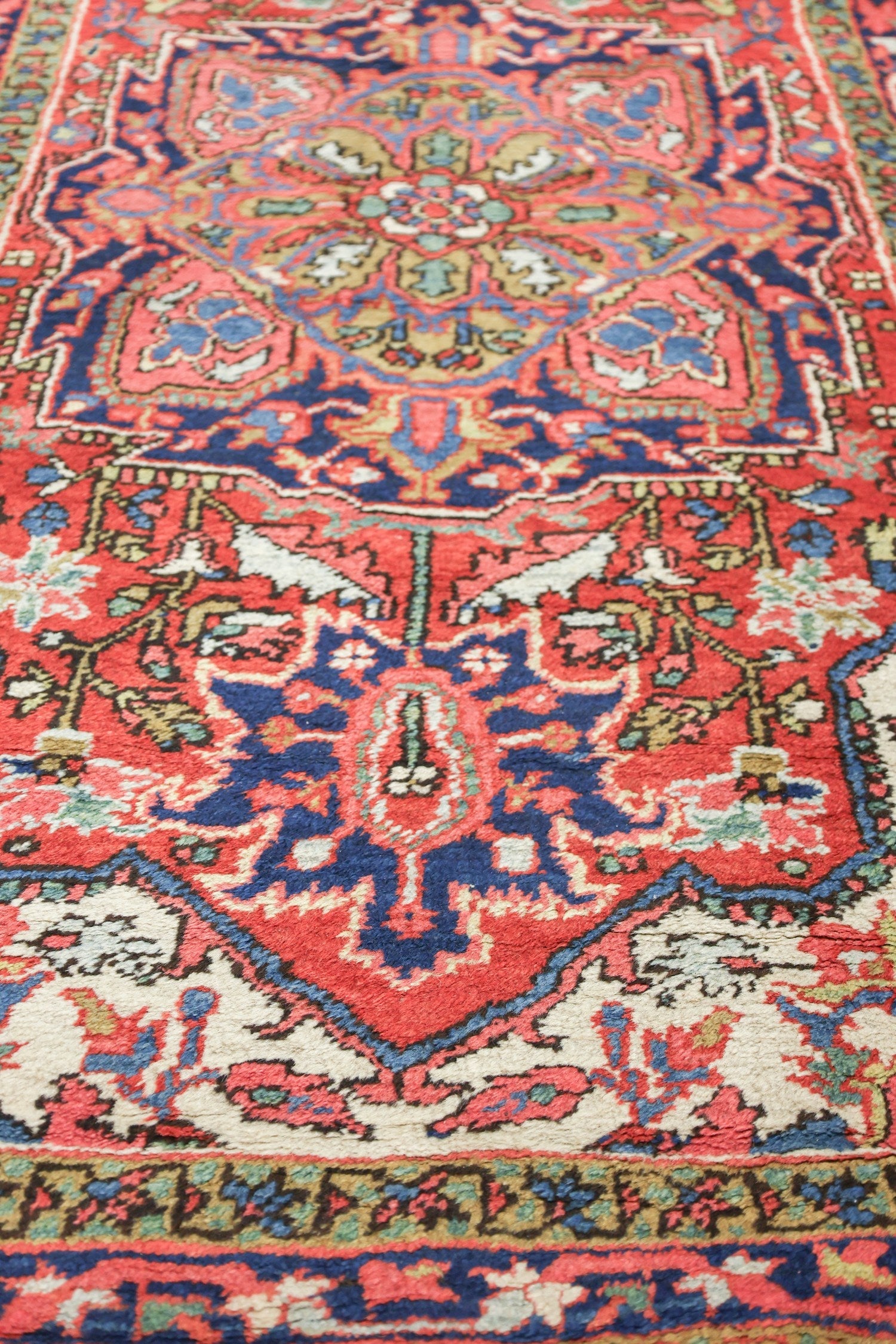 Intricate detail of a handwoven tribal rug, showcasing a vibrant red base with navy blue and beige floral patterns.
