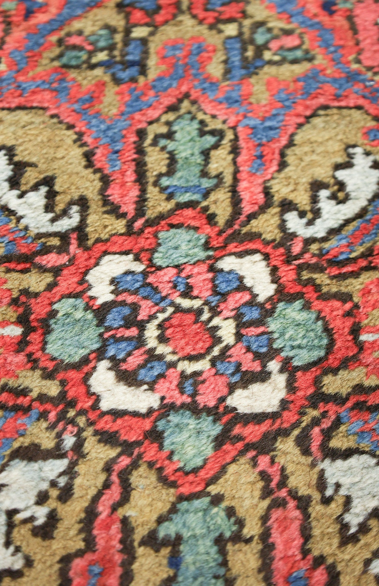 Close-up of antique tribal rug detail, showcasing handwoven floral pattern in red, blue, and beige.
