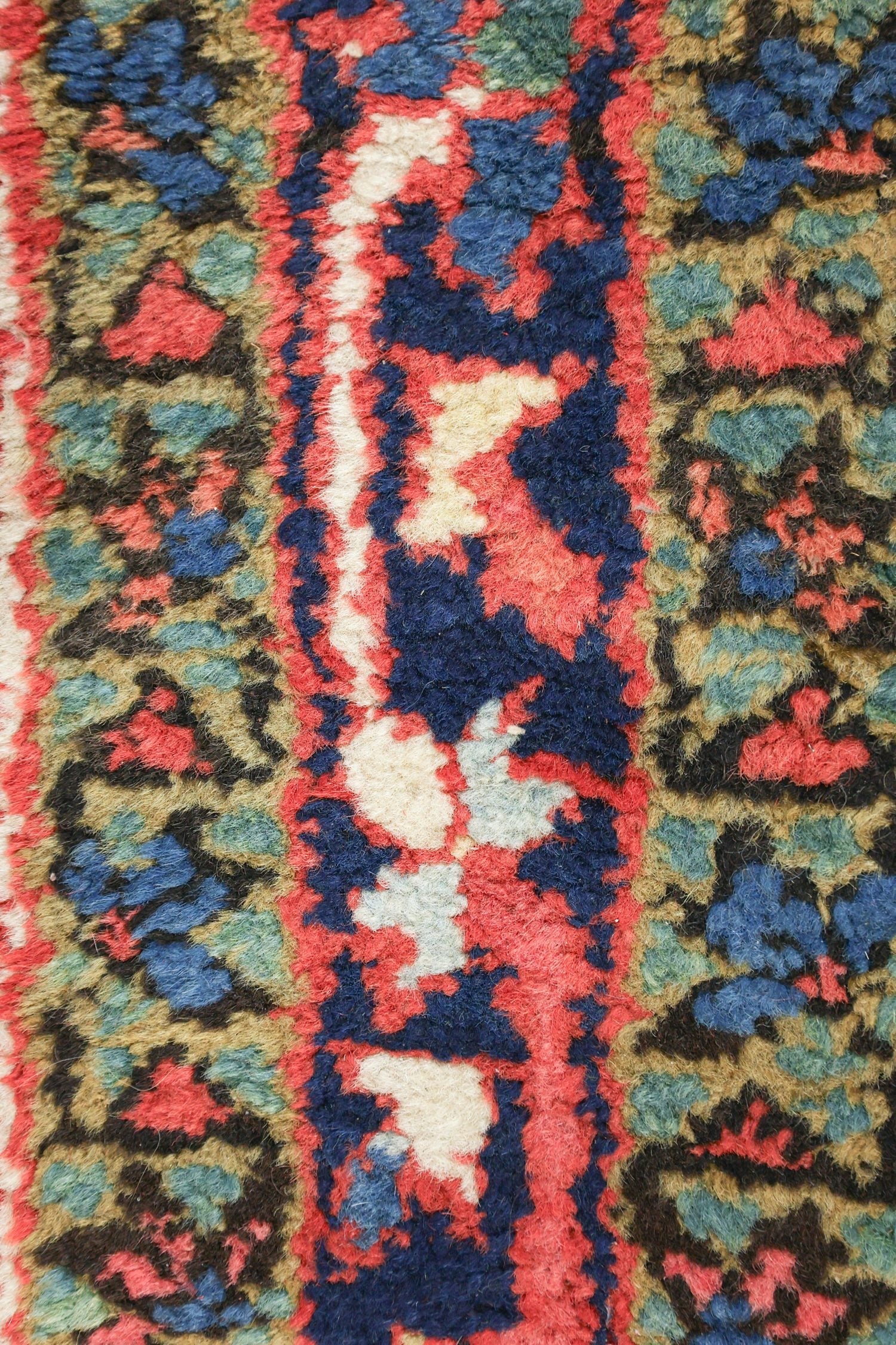 Close-up of a handwoven rug's detailed, colorful pattern in reds, blues, and greens.
