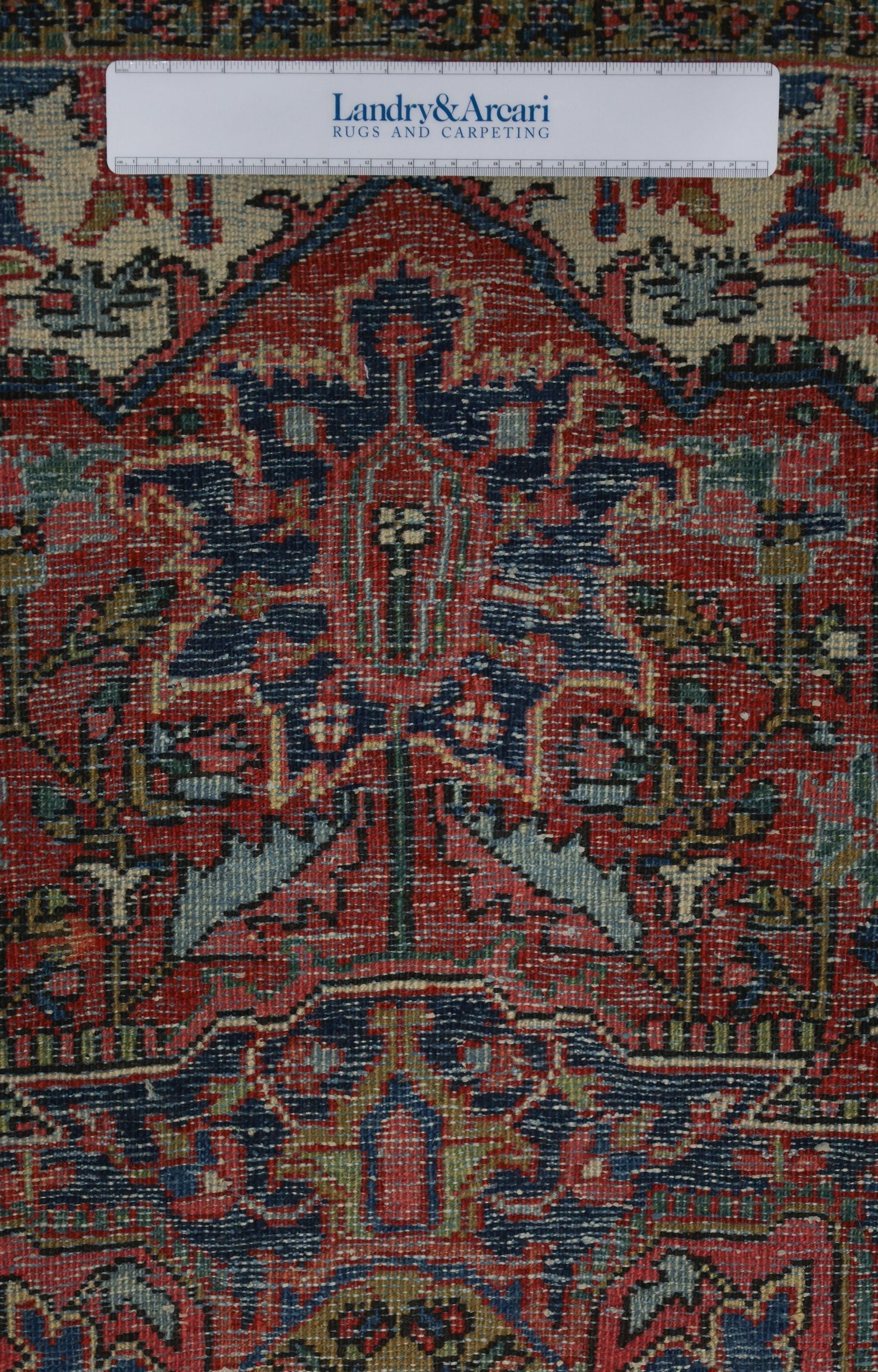 Close-up detail of an antique rug's intricate, handwoven pattern in red, blue, and beige.
