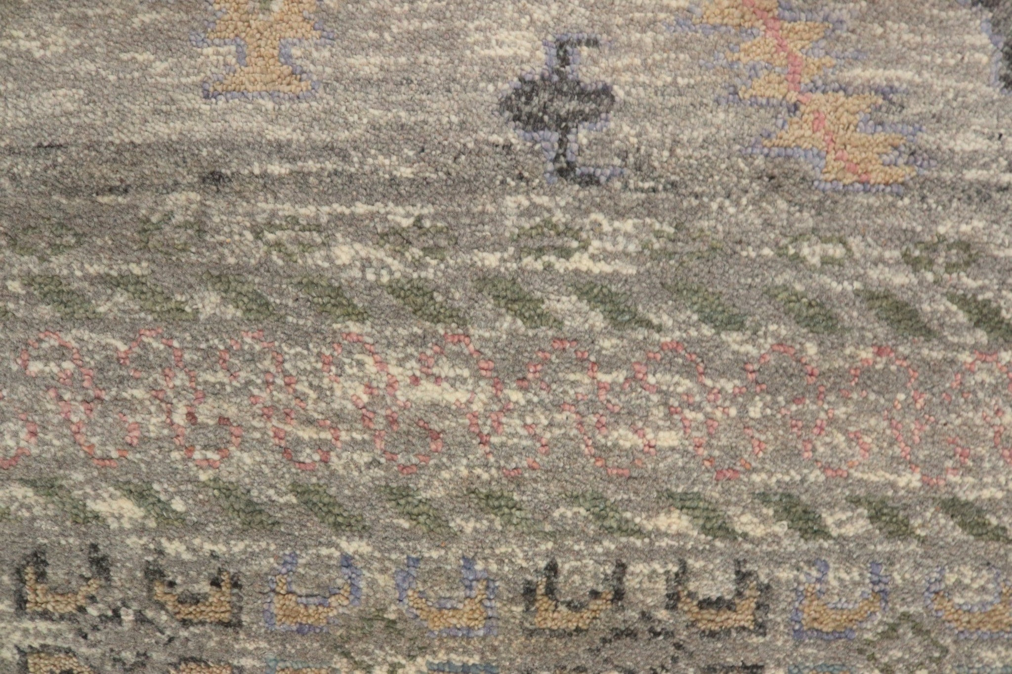 Close-up of handwoven rug detail, showcasing muted grey, pink, and green tones in a tribal pattern.
