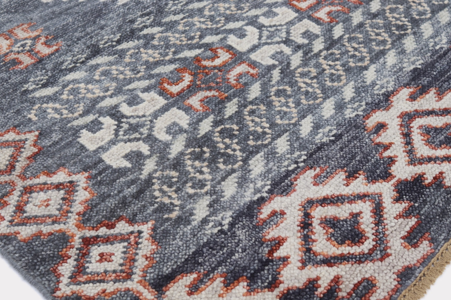 Close-up of handwoven rug displaying gray, cream, and burnt orange tribal patterns.
