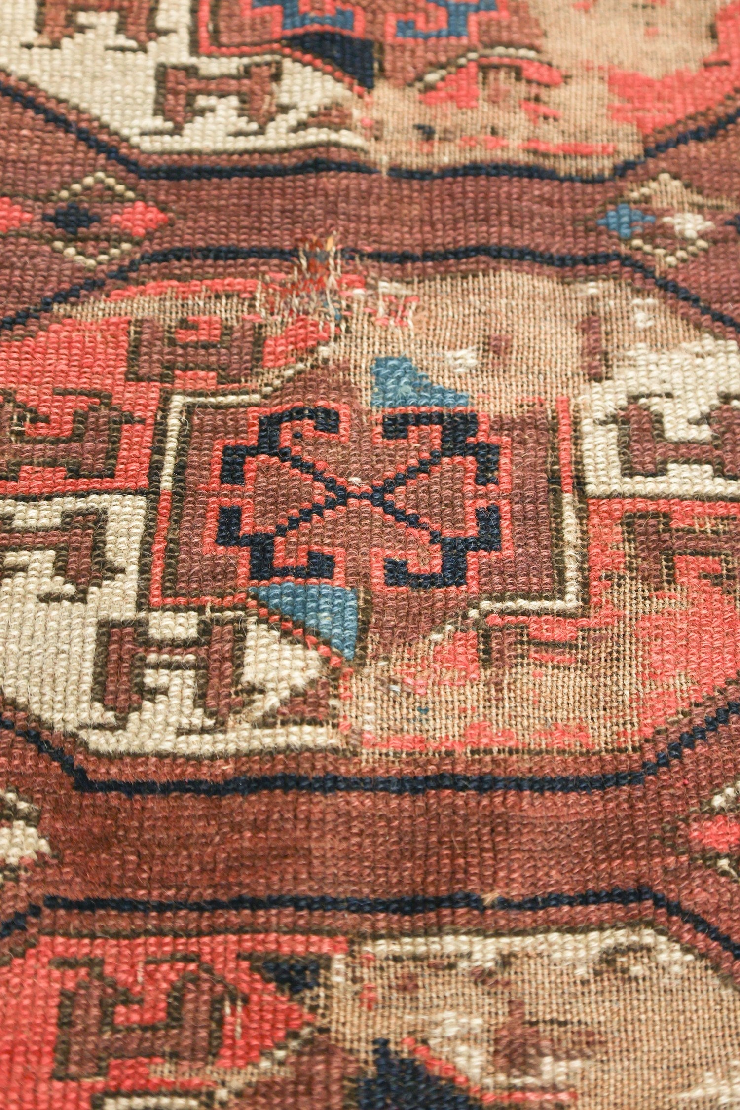 Close-up detail of a handwoven rug, showcasing its intricate red, beige, and navy pattern.
