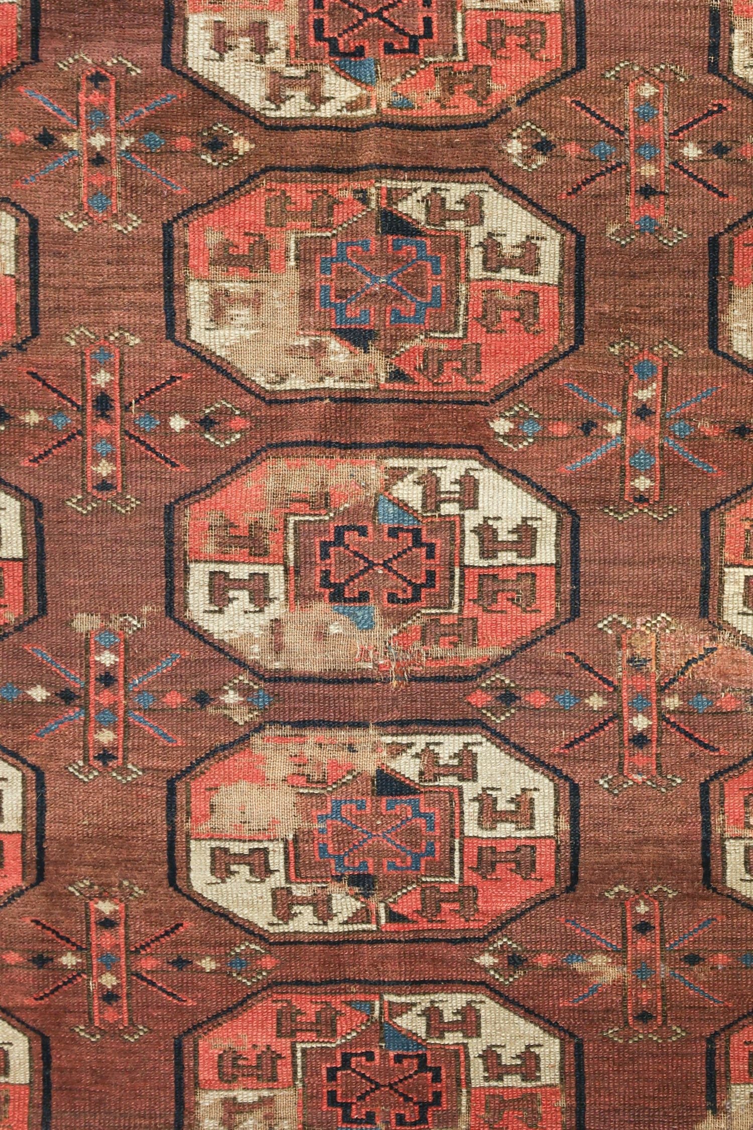 Handwoven tribal rug detail, showcasing an antique, reddish-brown design with geometric patterns.
