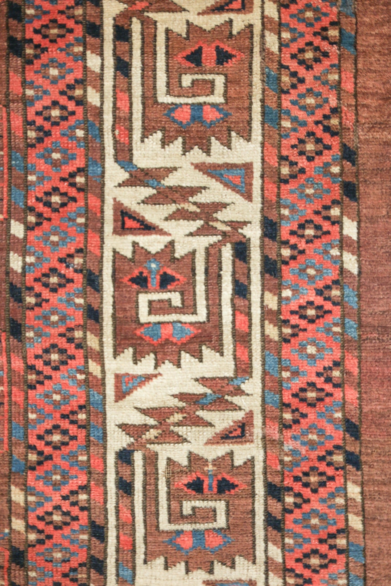 Close-up of antique rug detail, showcasing handwoven tribal pattern in red, blue, and brown tones.
