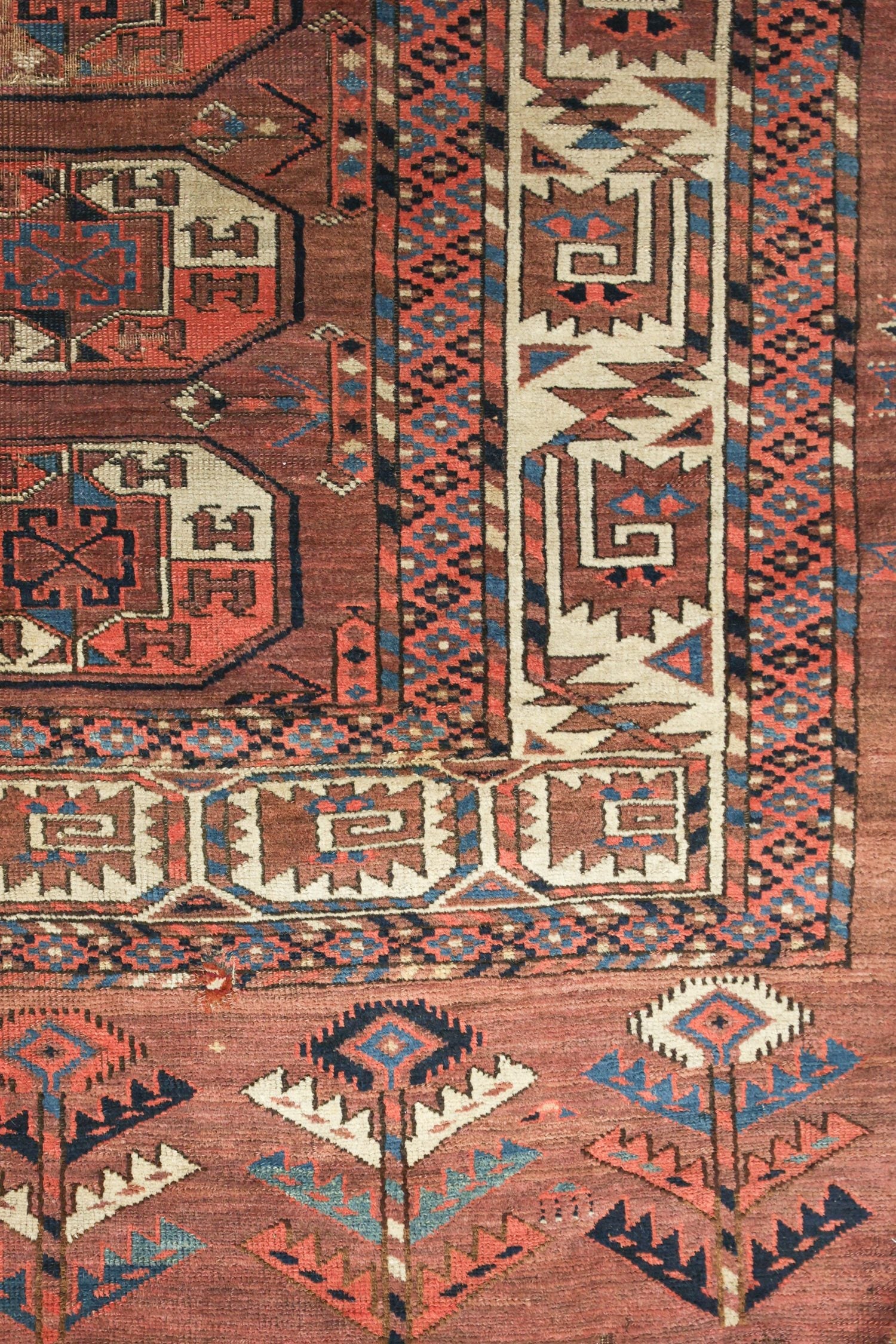 Detail of an antique handwoven rug, showcasing intricate geometric and floral patterns in red, blue, and beige.
