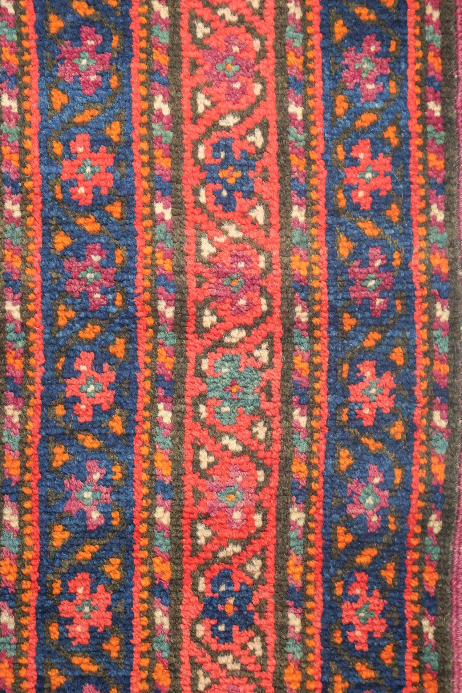 Close-up of antique Azeri rug's vibrant, handwoven floral pattern in red, blue, and orange.
