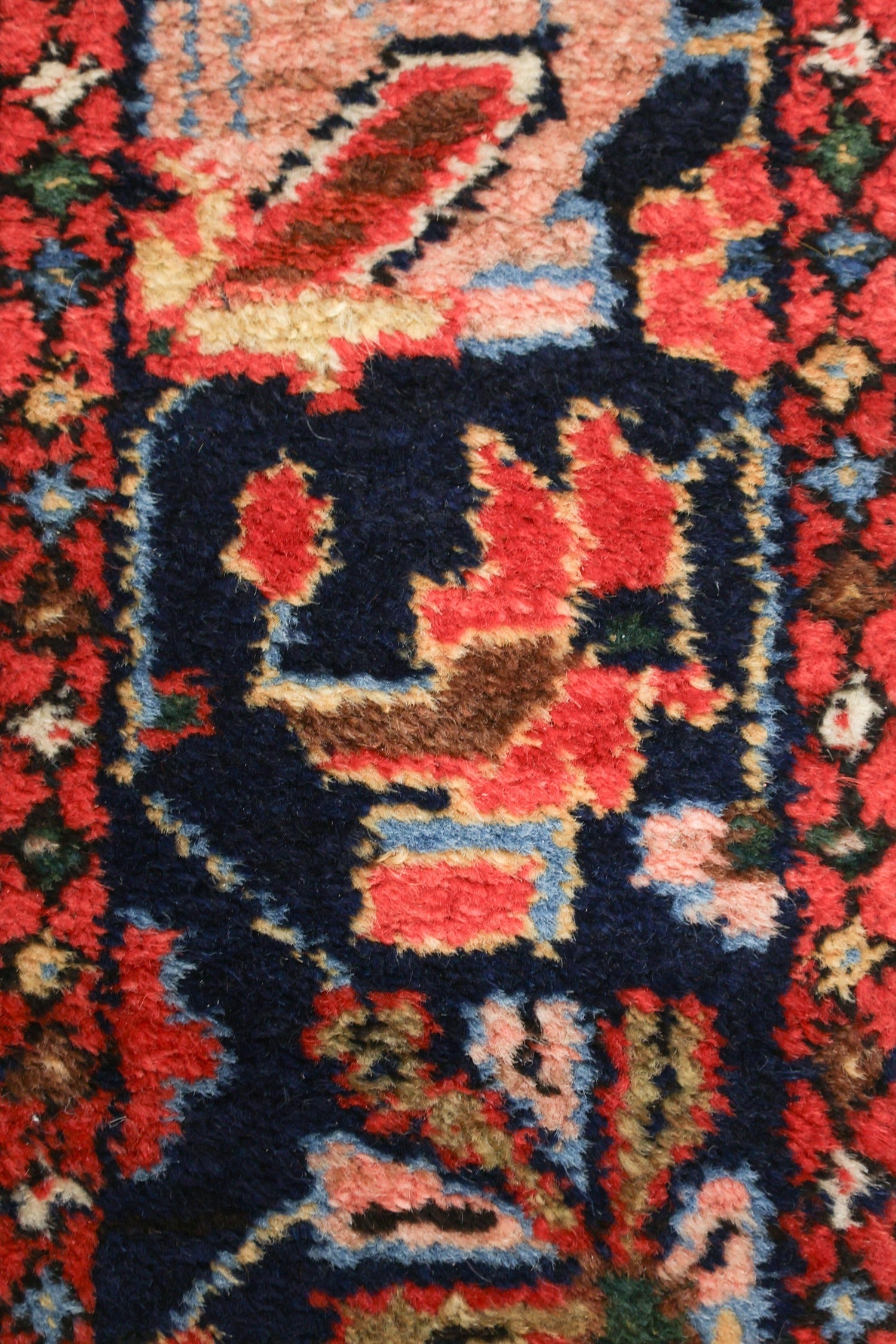 Close-up view of a richly colored handwoven rug, showcasing intricate details in red, blue, and beige tones.
