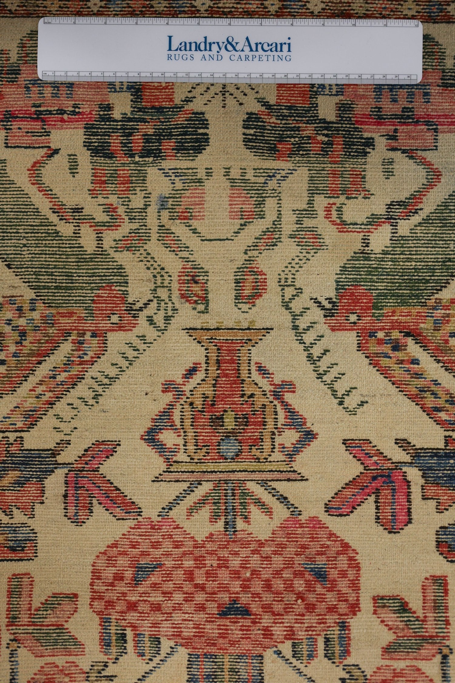 Detailed close-up of antique Bakhtiari rug, showcasing intricate floral and vase motifs in red, green, and blue on a cream background.
