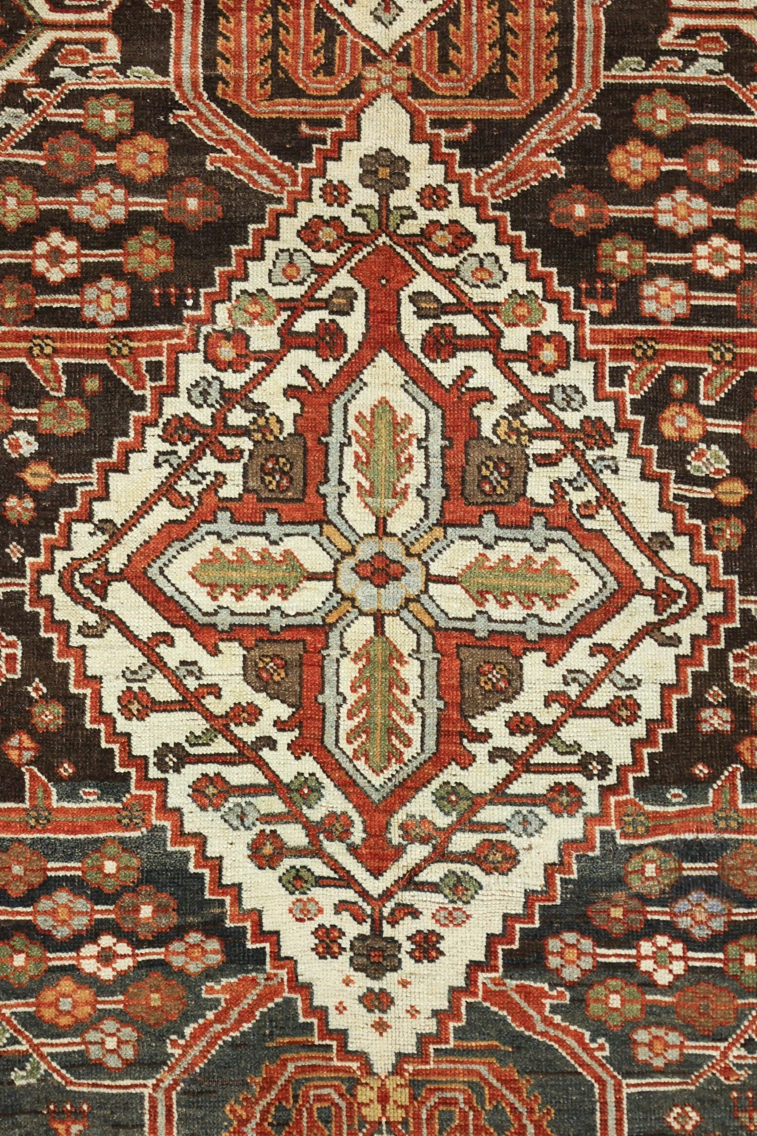 Close-up detail of an antique rug's intricate, handwoven floral pattern in muted reds, greens, and creams on a dark background.
