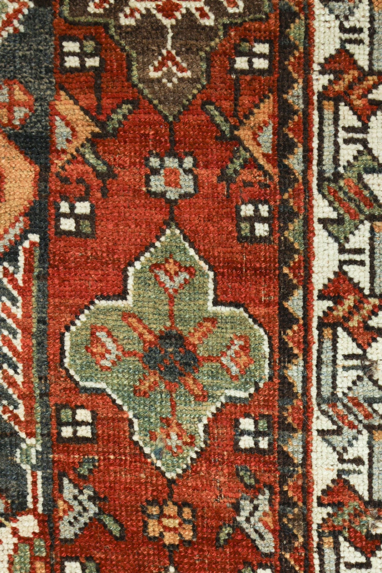 Close-up detail of a handwoven rug's intricate, red and green pattern.
