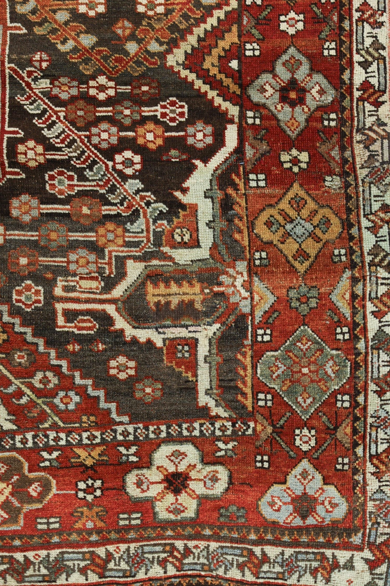 Detail of antique Bakhtiari rug, showcasing intricate handwoven floral and geometric patterns in red, dark brown, and off-white.
