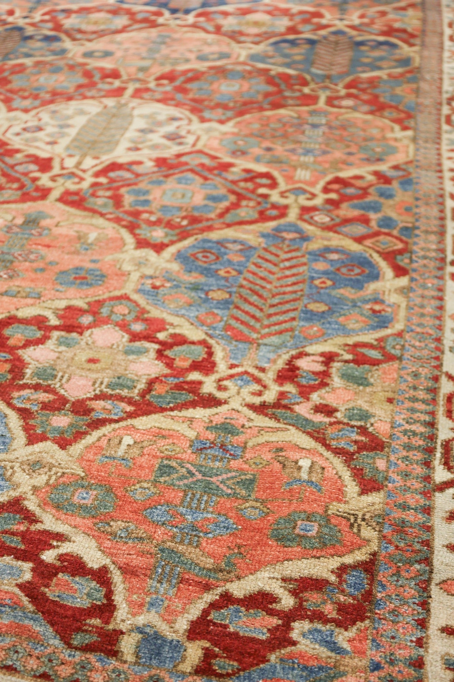 Close-up of an antique rug's intricate, handwoven design in red, blue, and beige.
