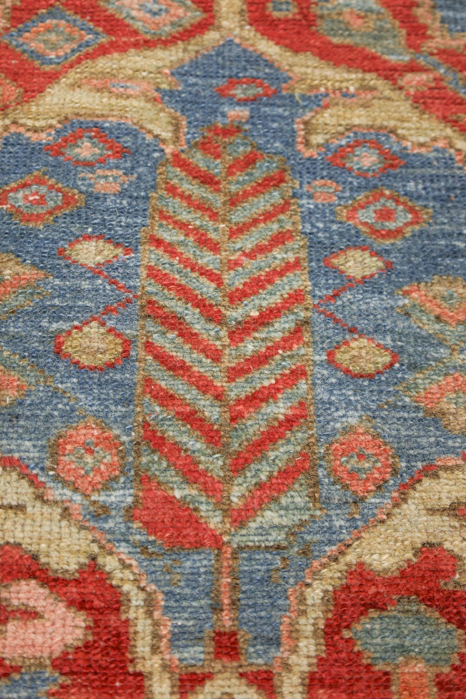 Close-up detail of a handwoven rug's intricate, red, blue, and beige pattern.
