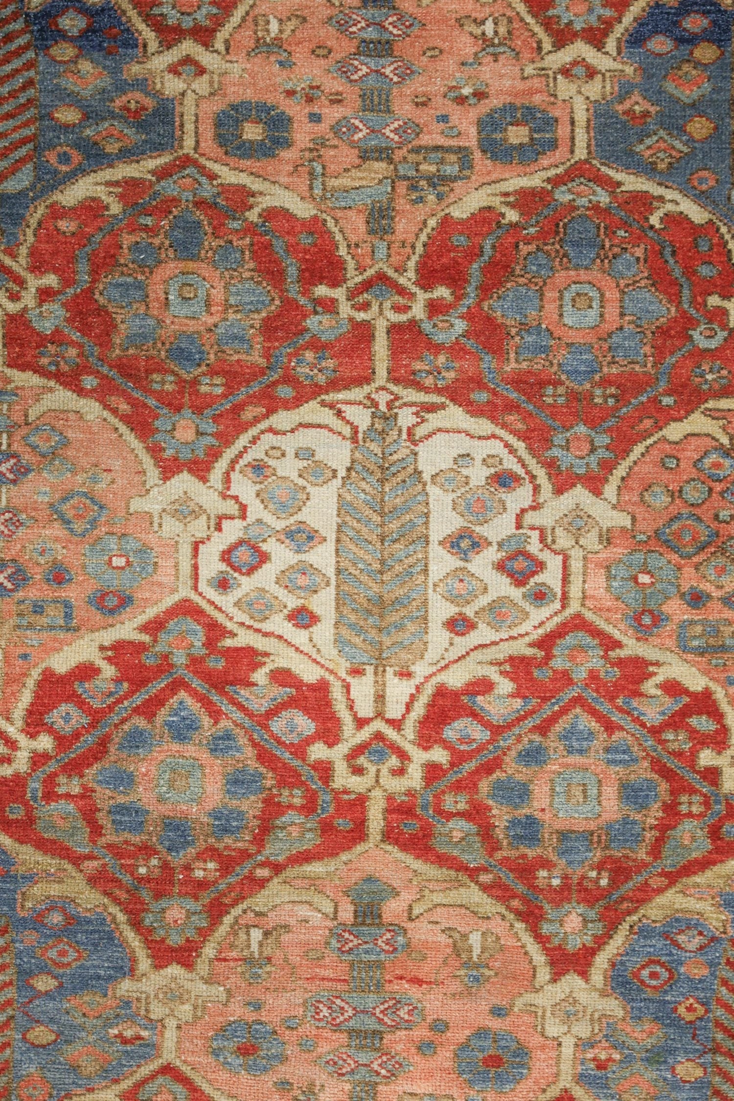 Detail of antique handwoven rug, featuring intricate red, blue, and beige floral patterns.
