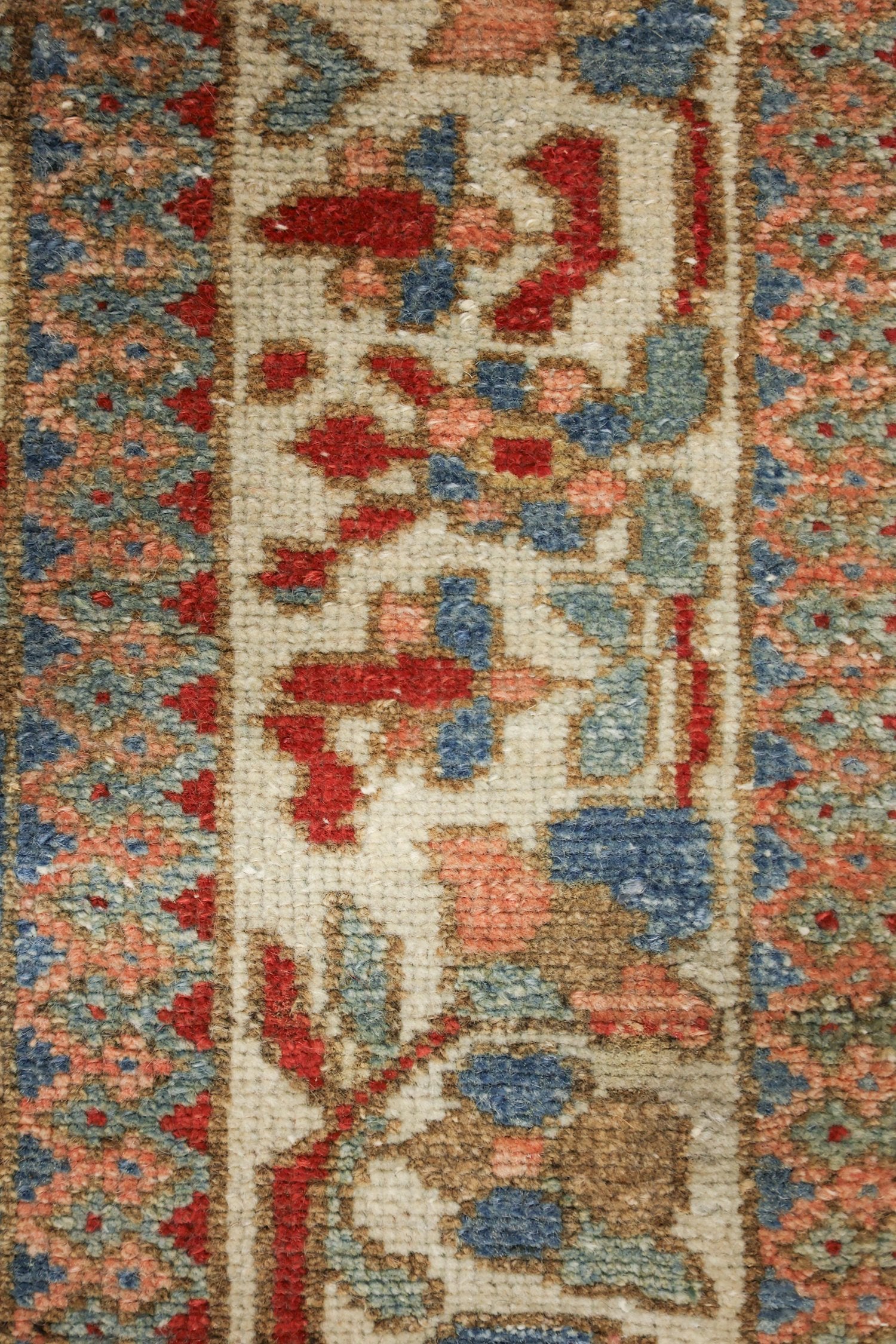 Close-up of antique rug's intricate handwoven floral pattern in muted reds, blues, and beige.
