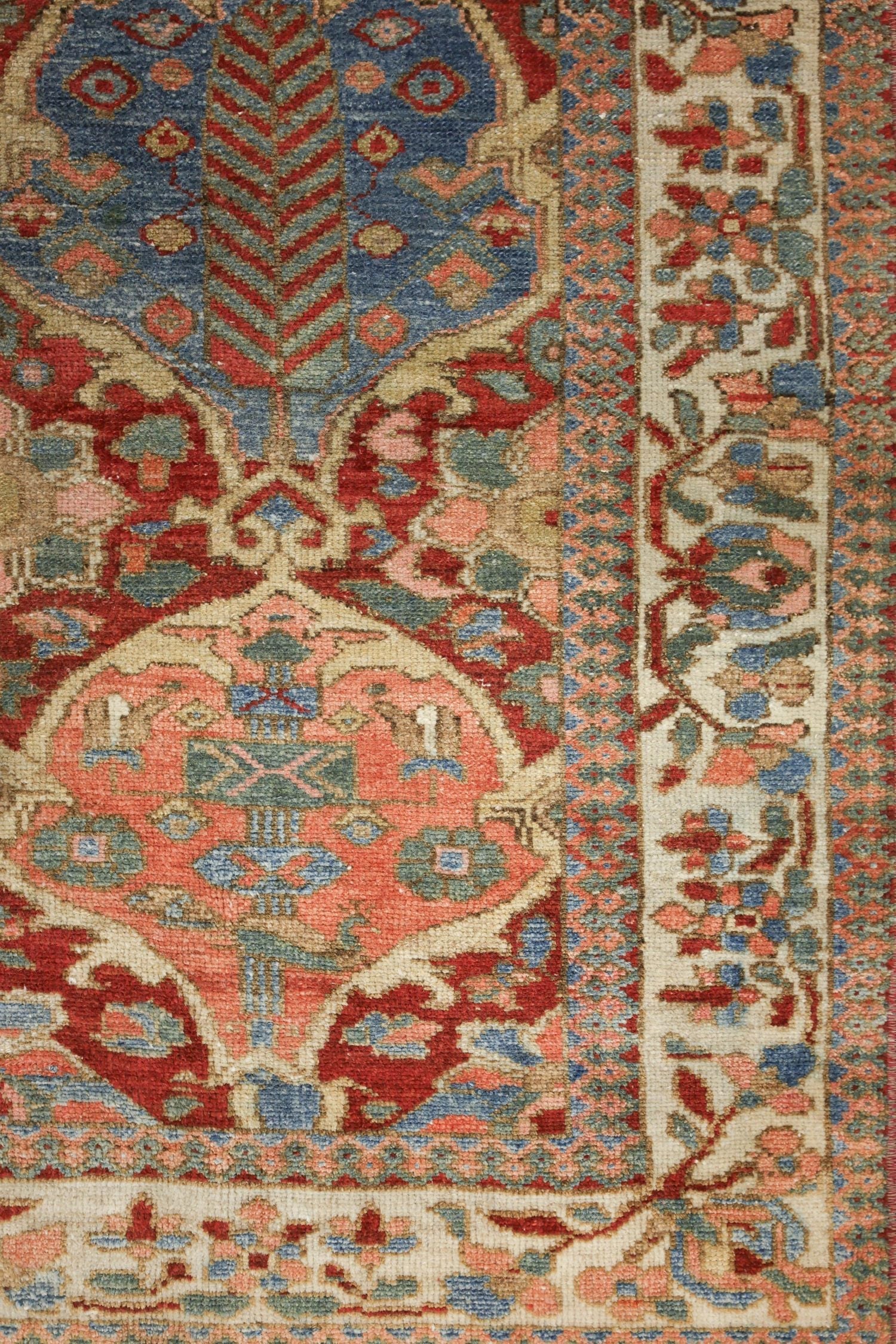 Detail of antique handwoven rug showcasing intricate floral and geometric patterns in red, blue, and beige.
