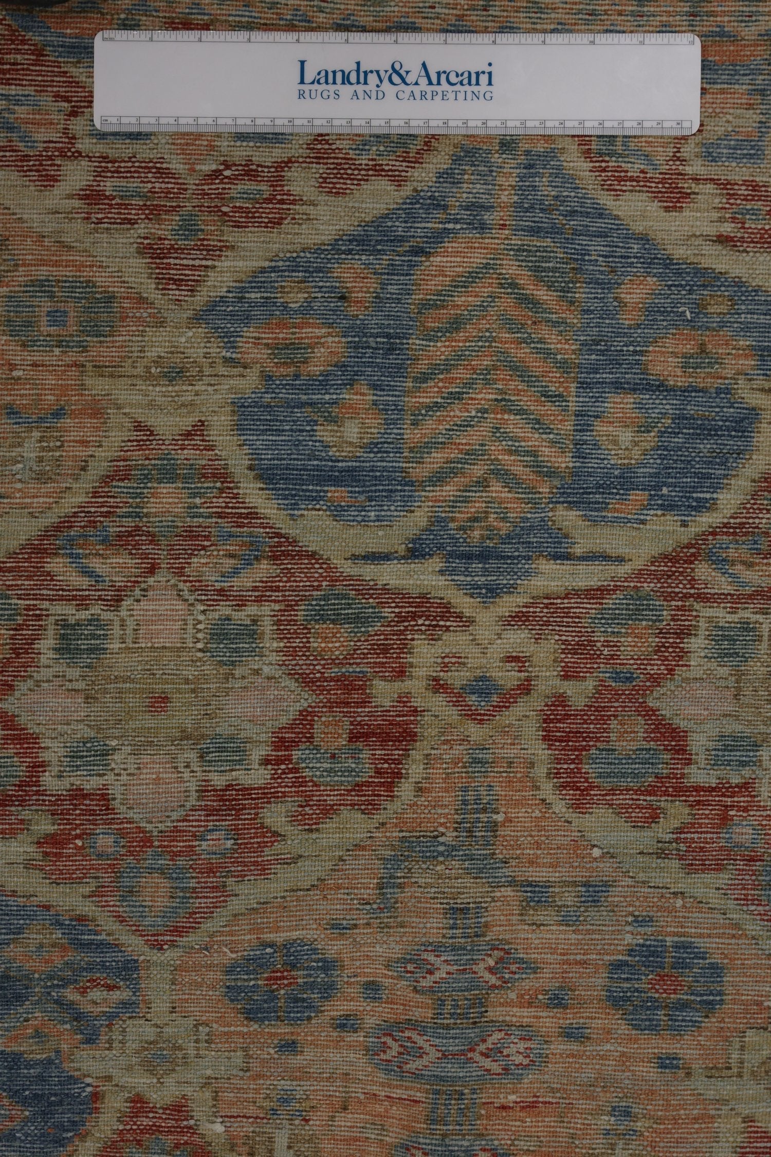 Close-up of antique rug detail, showcasing handwoven design in muted reds, blues, and beige.
