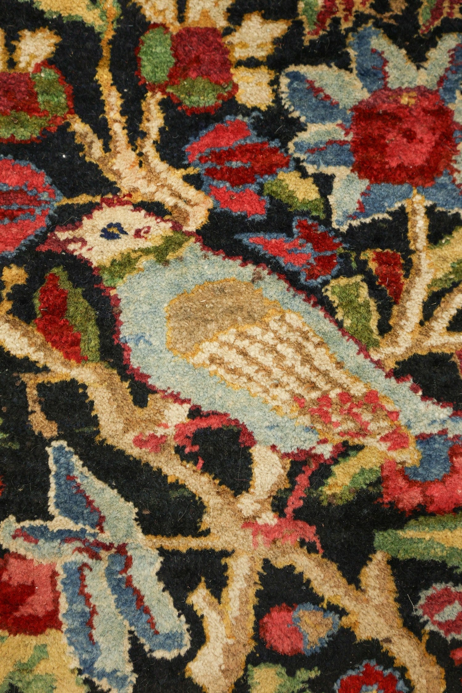 Close-up of antique rug detail: handwoven floral and bird pattern in red, blue, green, beige, and black.
