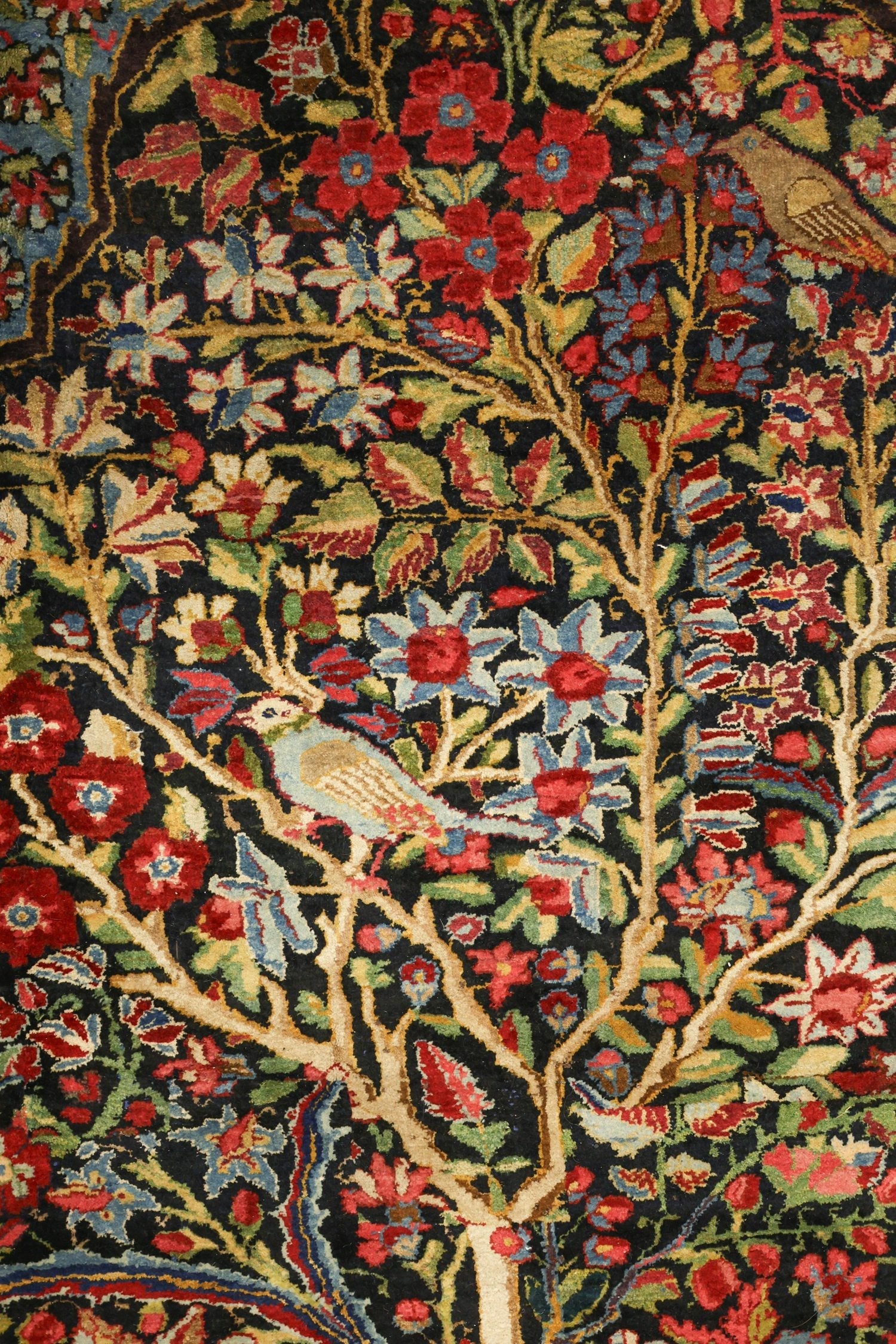 Handwoven rug detail: intricate floral and bird motifs on a dark background, antique Bakhtiari style.
