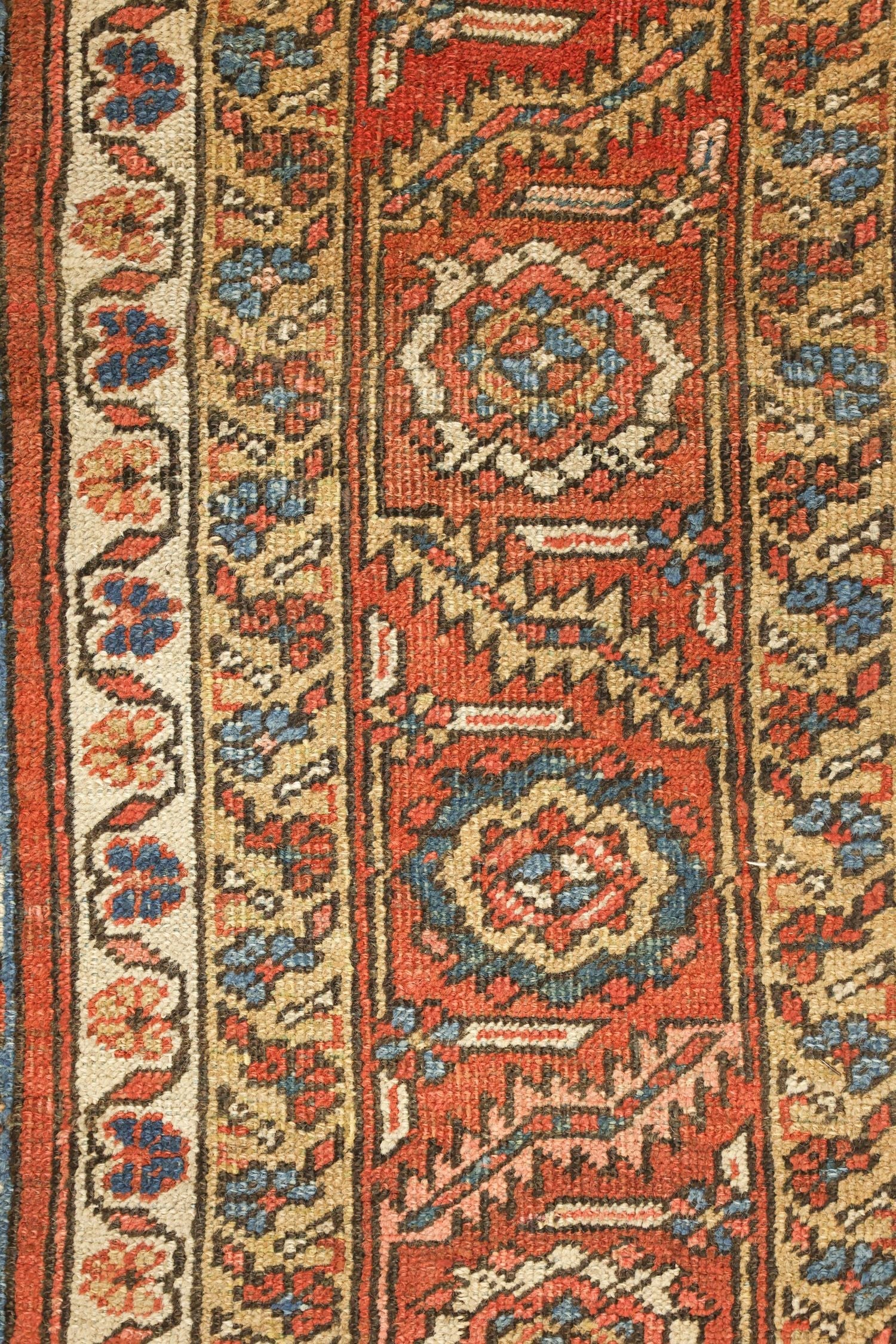 Close-up detail of a handwoven rug's intricate, red and beige floral pattern.
