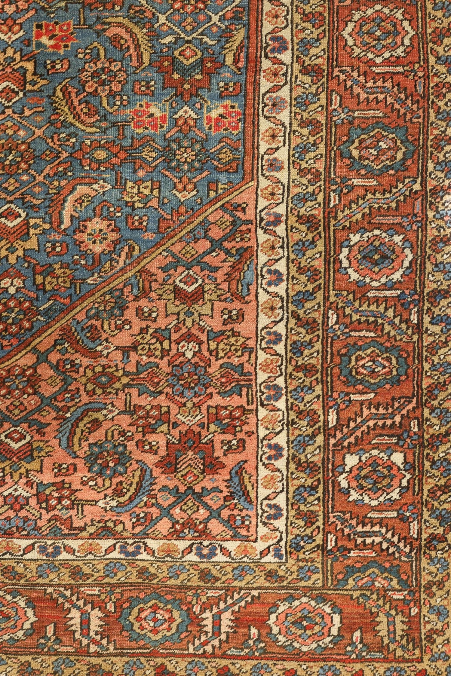 Detail of antique handwoven rug, showcasing intricate floral and geometric patterns in muted reds, blues, and beige.
