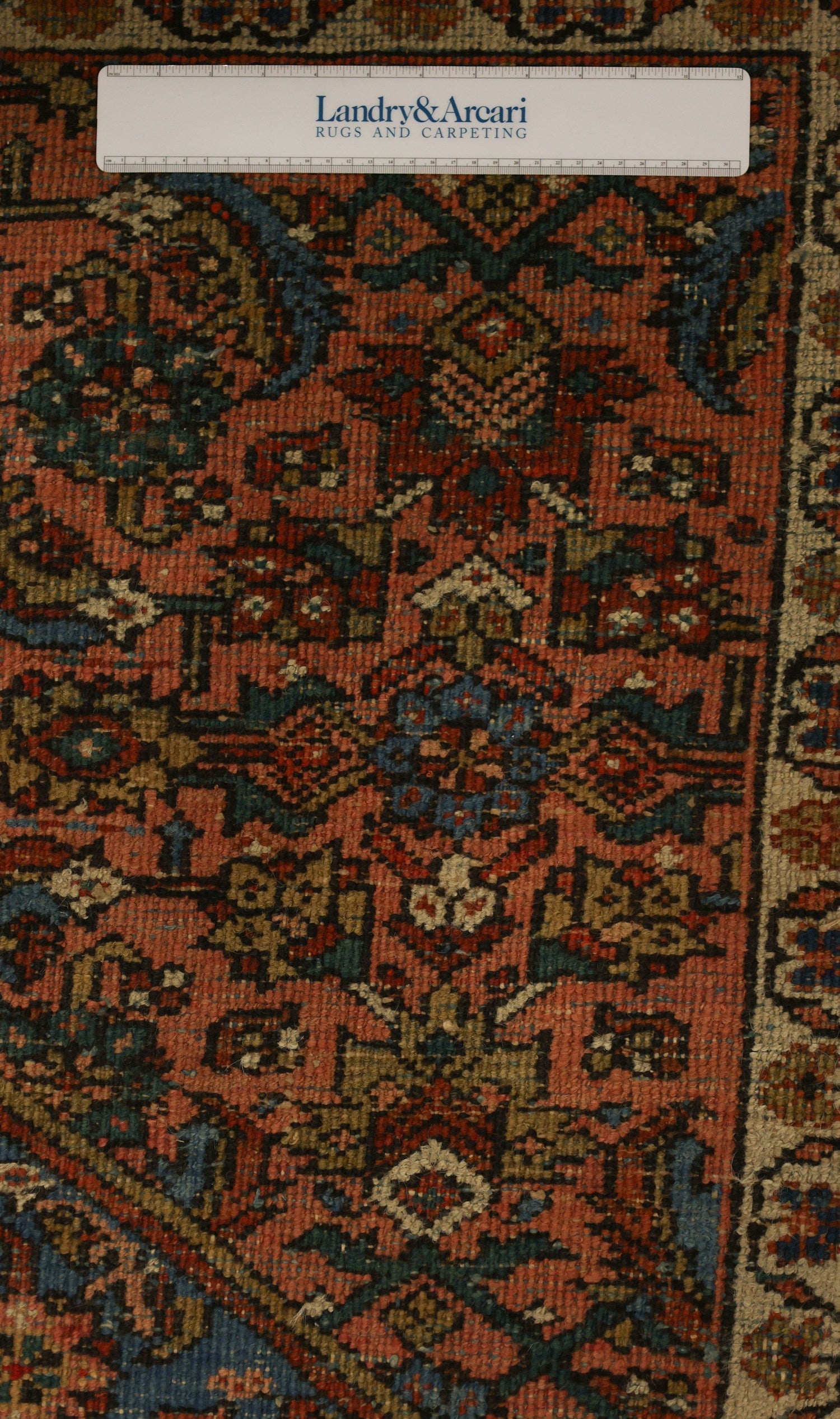 Close-up detail of antique handwoven rug, showcasing intricate red, blue, and gold pattern.
