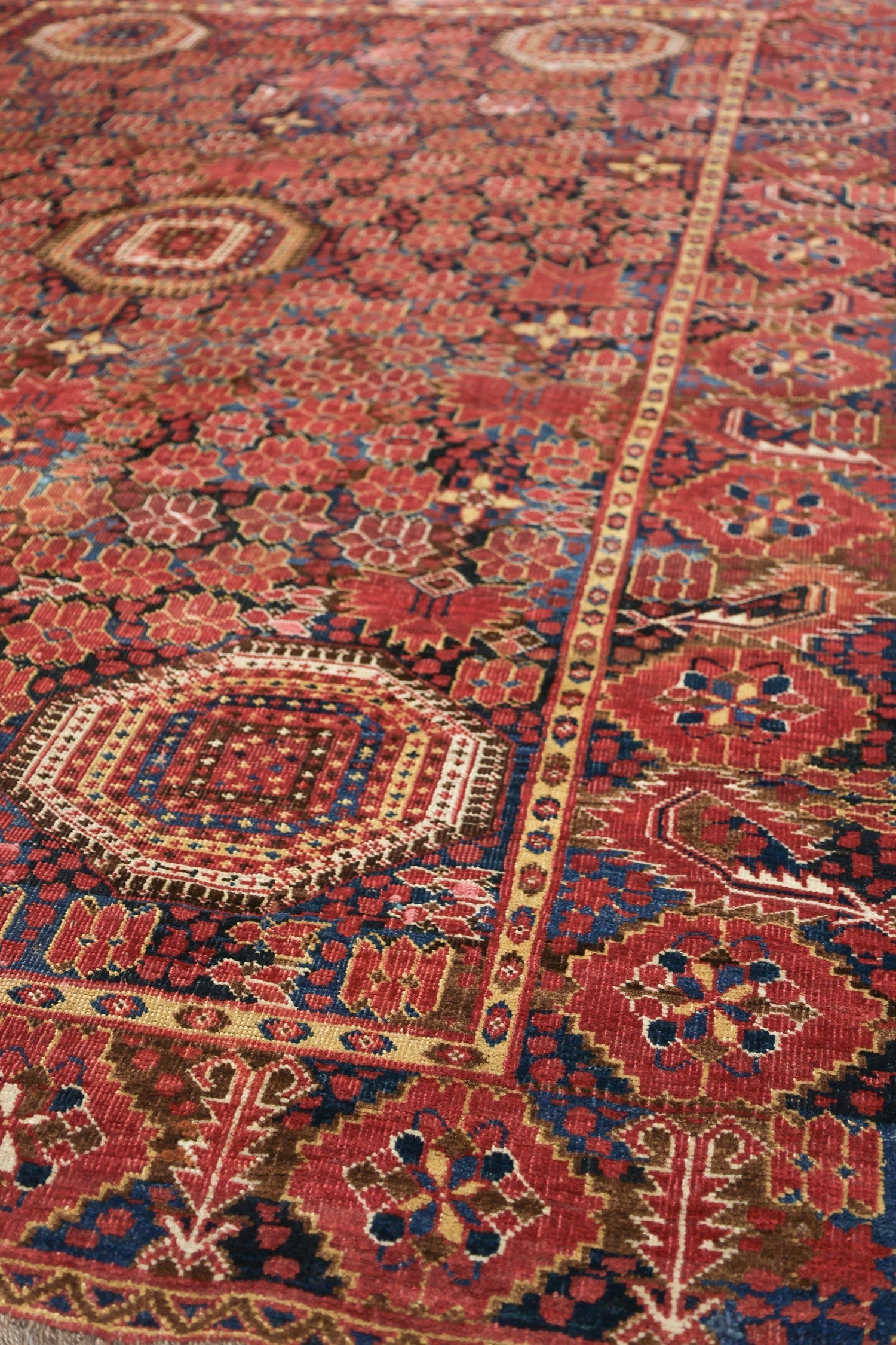 Detail of antique handwoven rug, rich red and blue tones, intricate tribal pattern.
