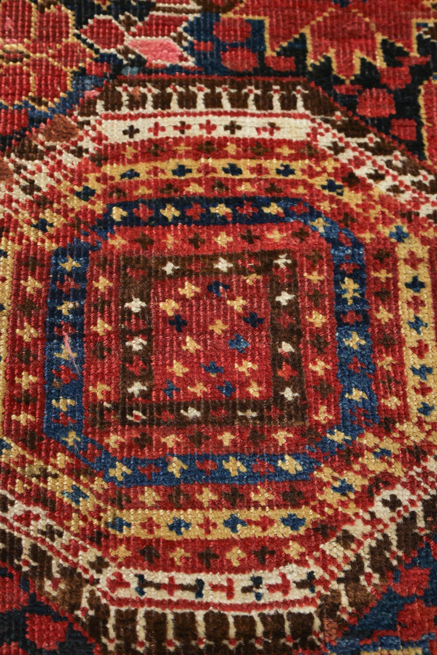 Close-up detail of antique rug's handwoven, red, blue, and brown pattern.
