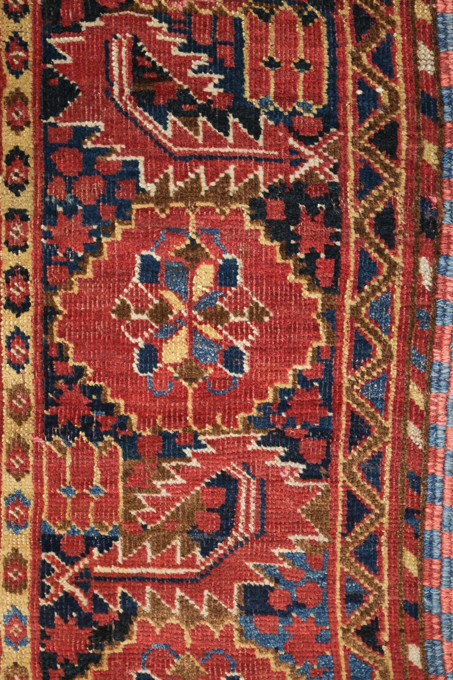 Close-up detail of a vintage handwoven rug, showcasing intricate red, blue, and beige patterns.
