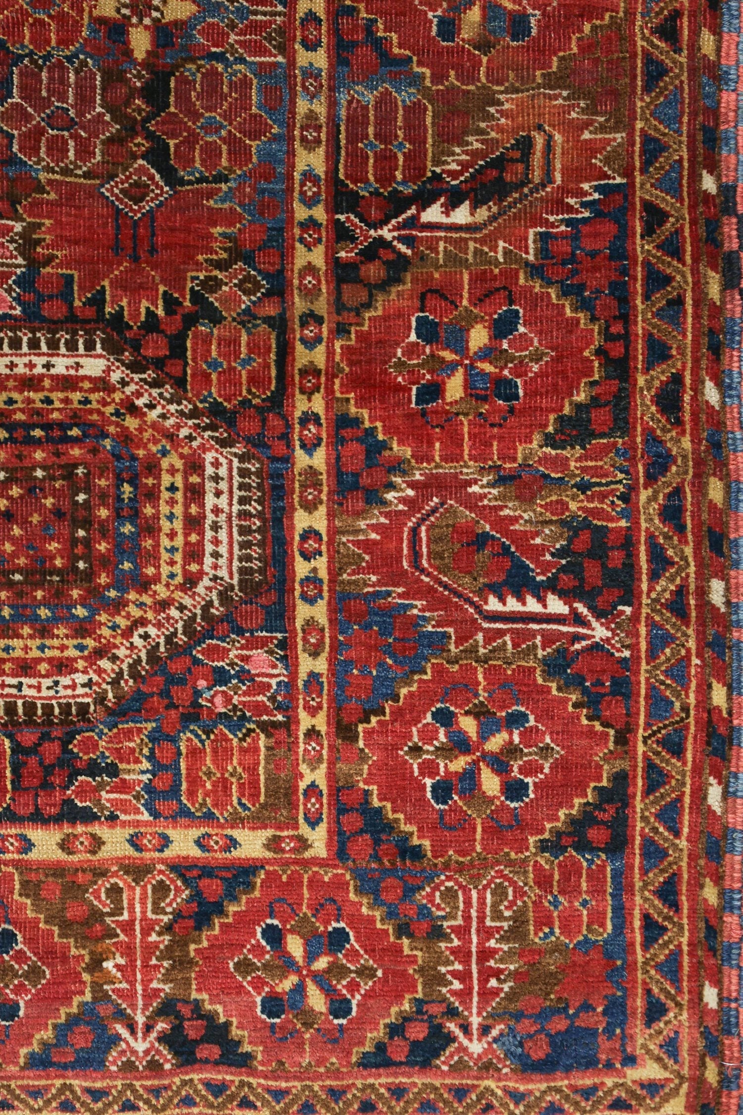 Detail of antique handwoven rug, rich red and navy tones, intricate tribal pattern.
