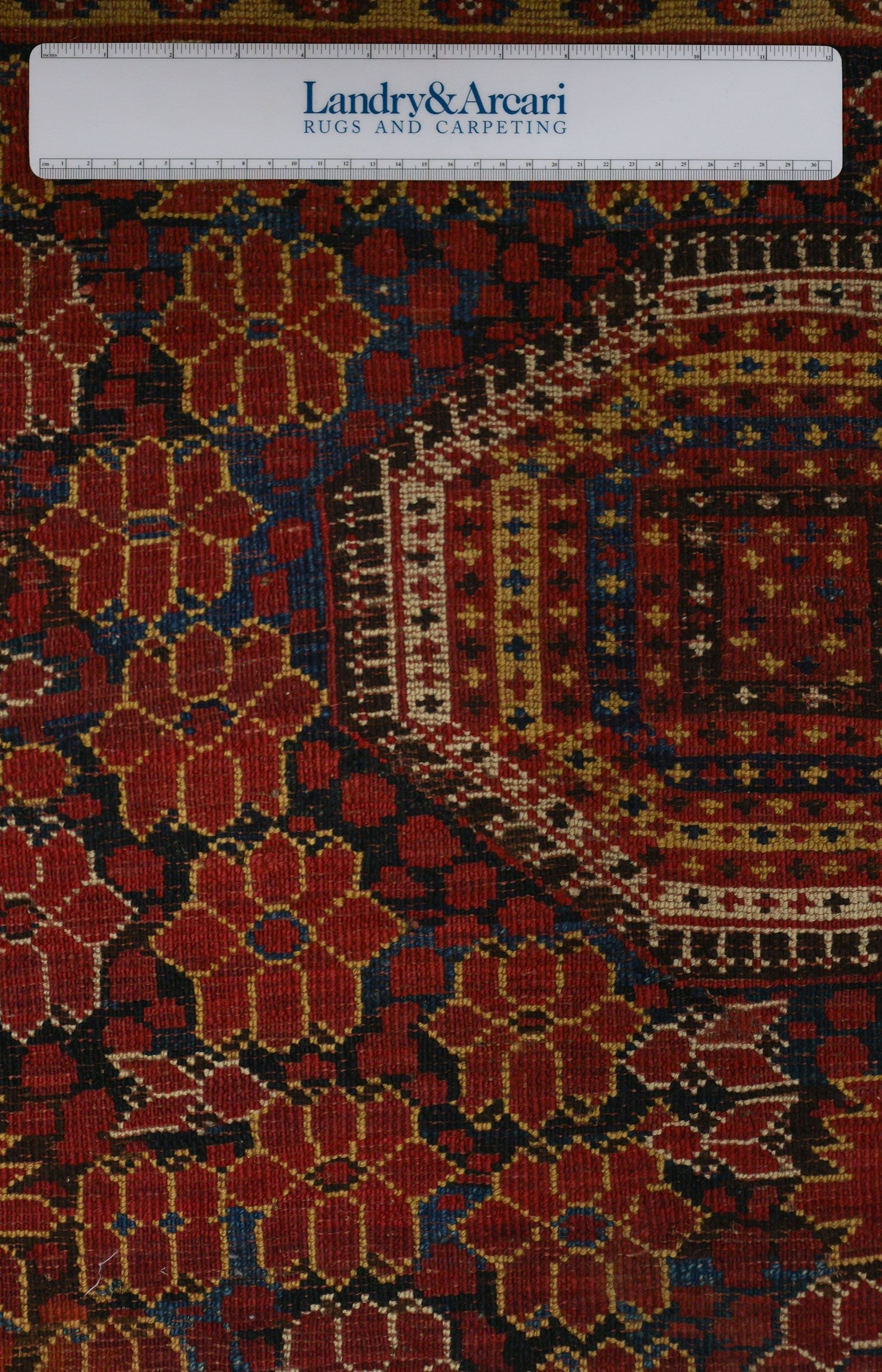 Close-up detail of a richly colored antique tribal rug, showcasing intricate handwoven patterns in red, blue, and gold.
