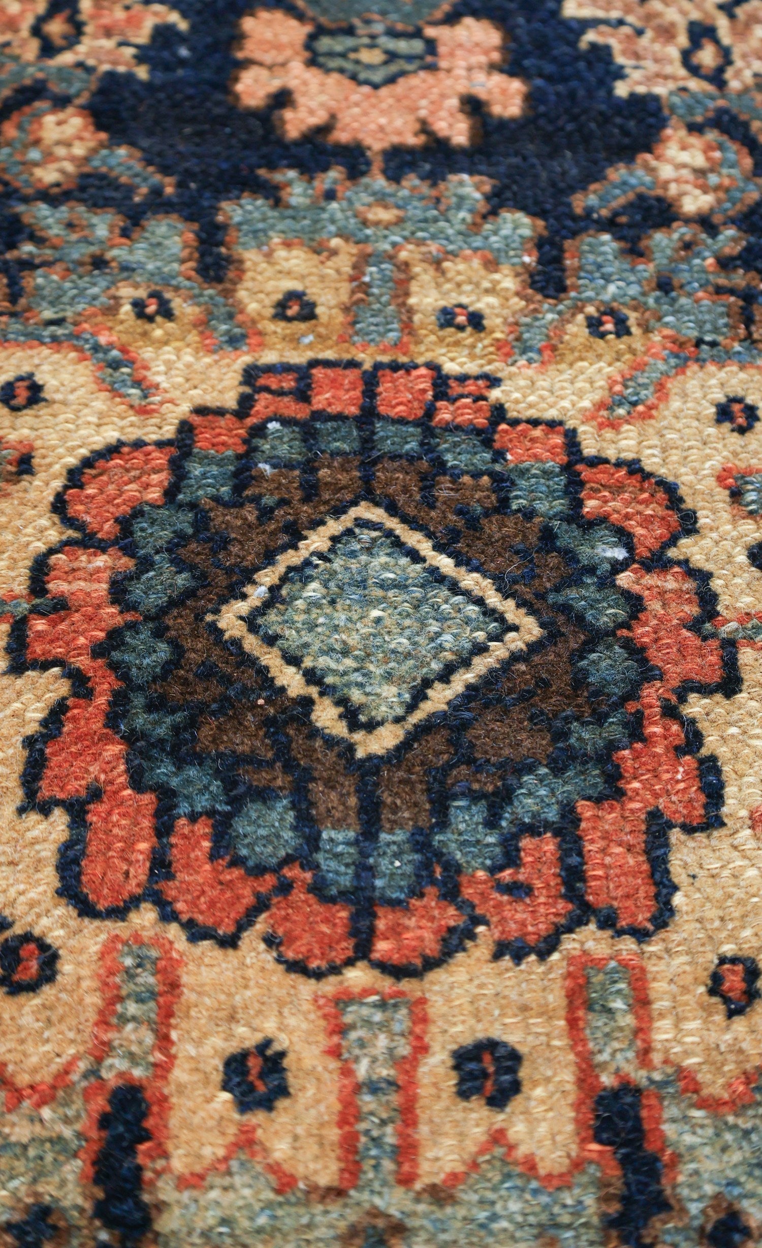 Close-up of antique rug detail, showcasing handwoven pattern in muted reds, blues, and beige.
